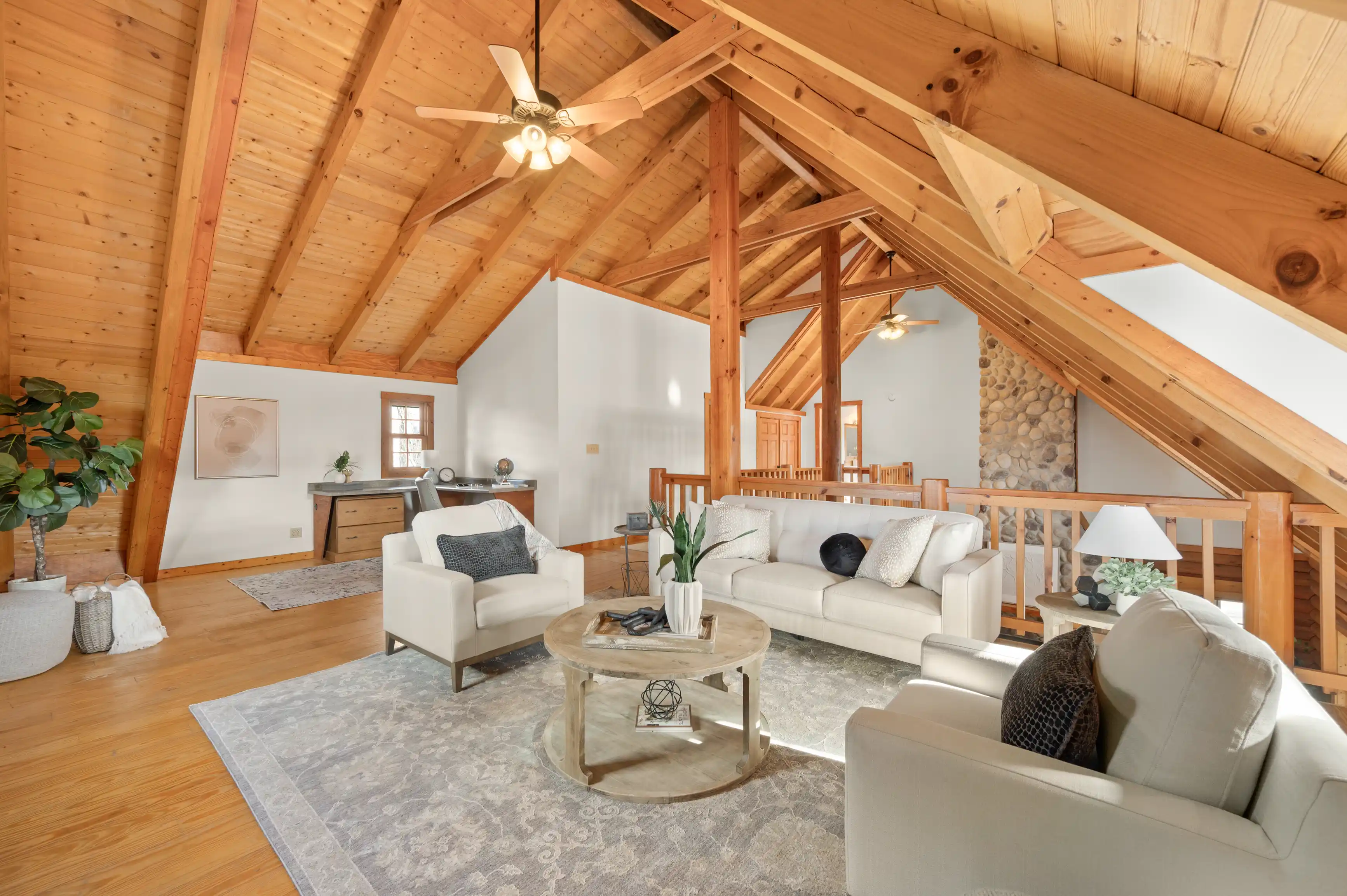 Spacious living room with high vaulted wooden ceilings, exposed beams, large windows, and comfortable furnishings including sofas and a round wooden coffee table.