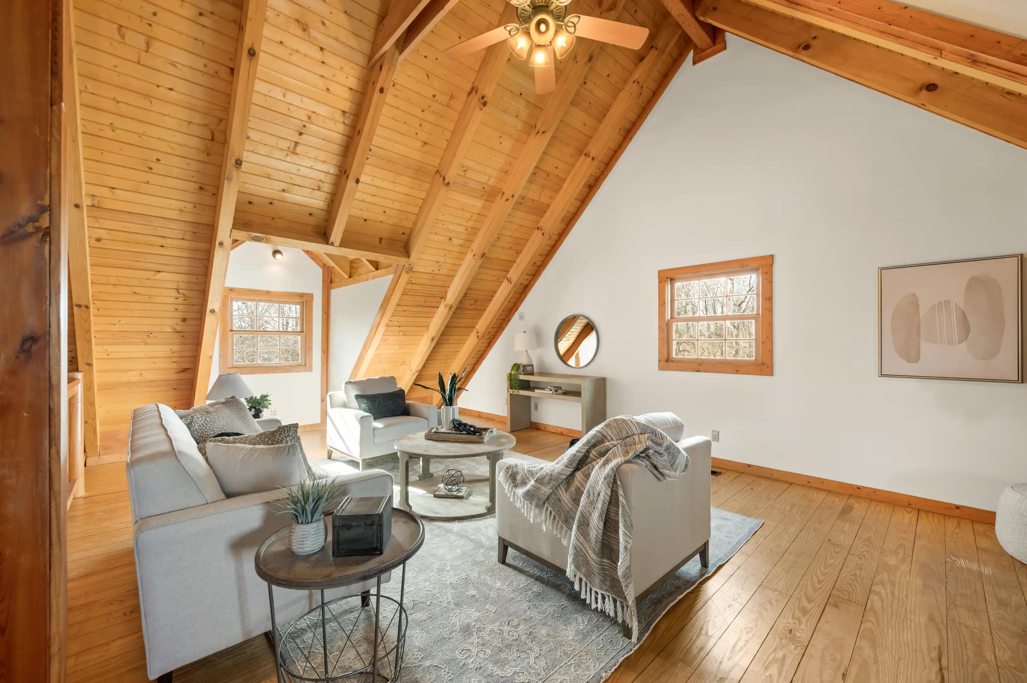 Cozy attic living room with wooden beam ceiling, hardwood floors, neutral toned furniture, and decorative accents.
