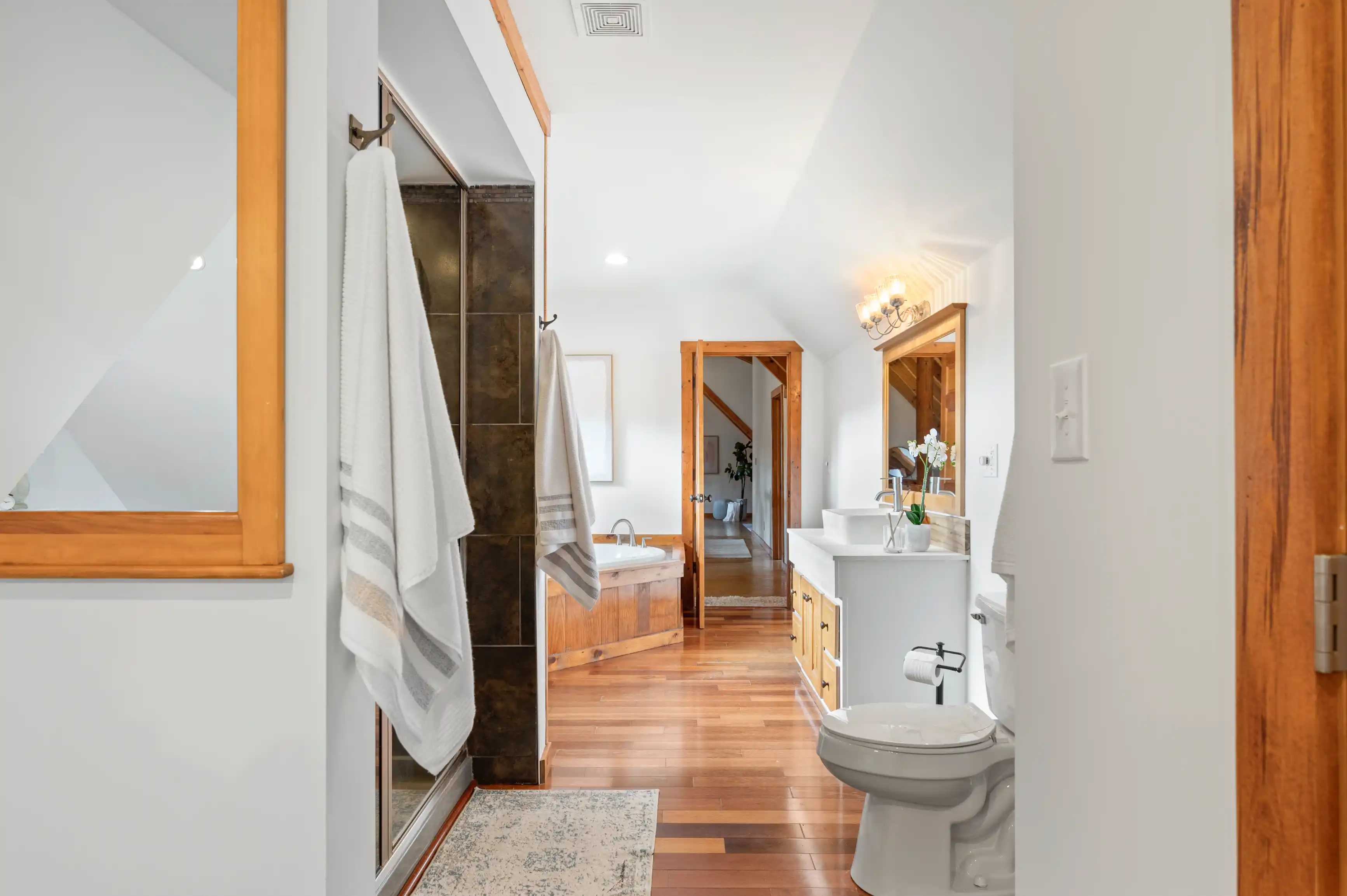 Modern bathroom interior with a glass shower, white vanity with a rectangular basin, wood frames and accents, and towels hanging on a rack by a mirror.