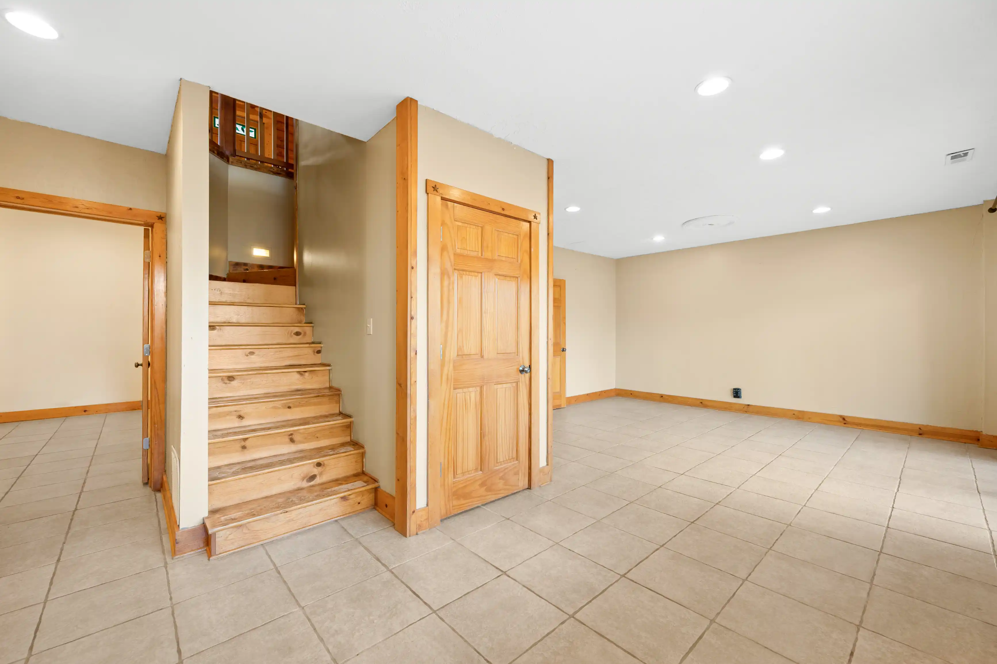 Spacious room with tile flooring, beige walls, wooden doors, and a staircase leading upstairs.