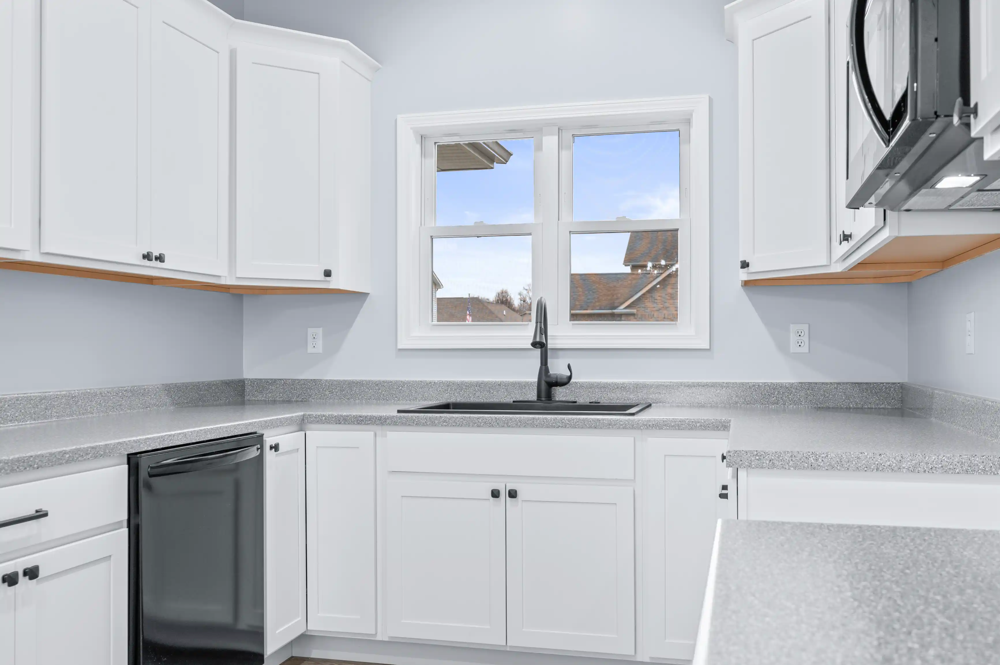 Modern kitchen interior with white cabinetry, granite countertops, and a window with a view of the sky and nearby rooftops.