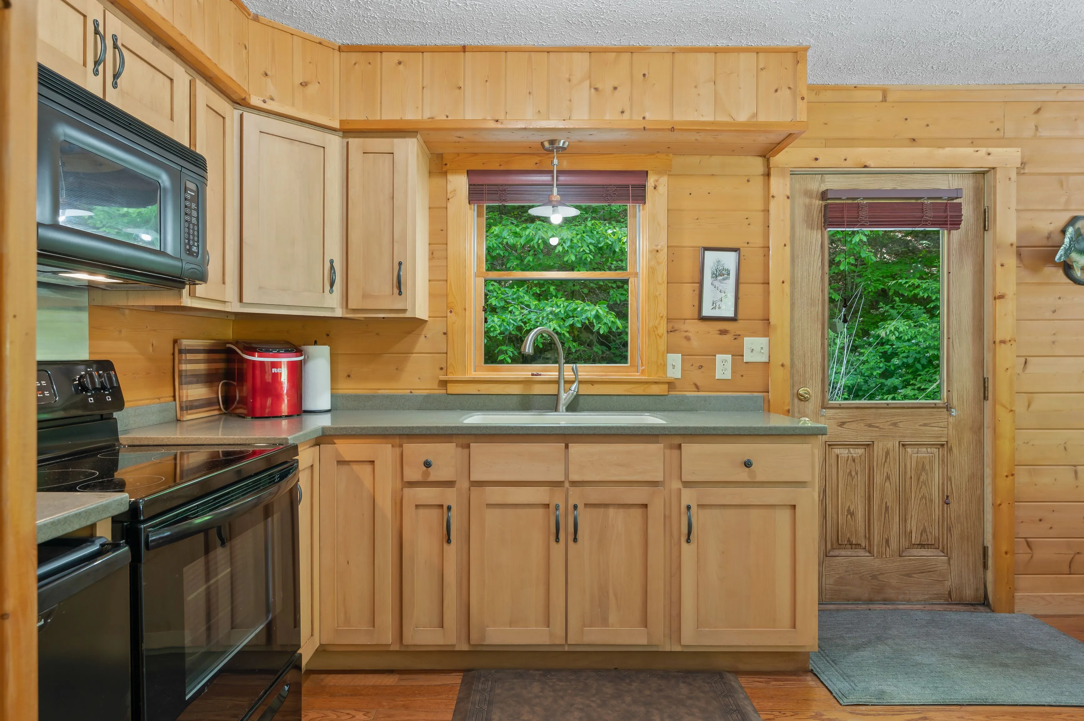 Cozy wooden kitchen interior with cabinets, countertops, and a window view of green foliage.