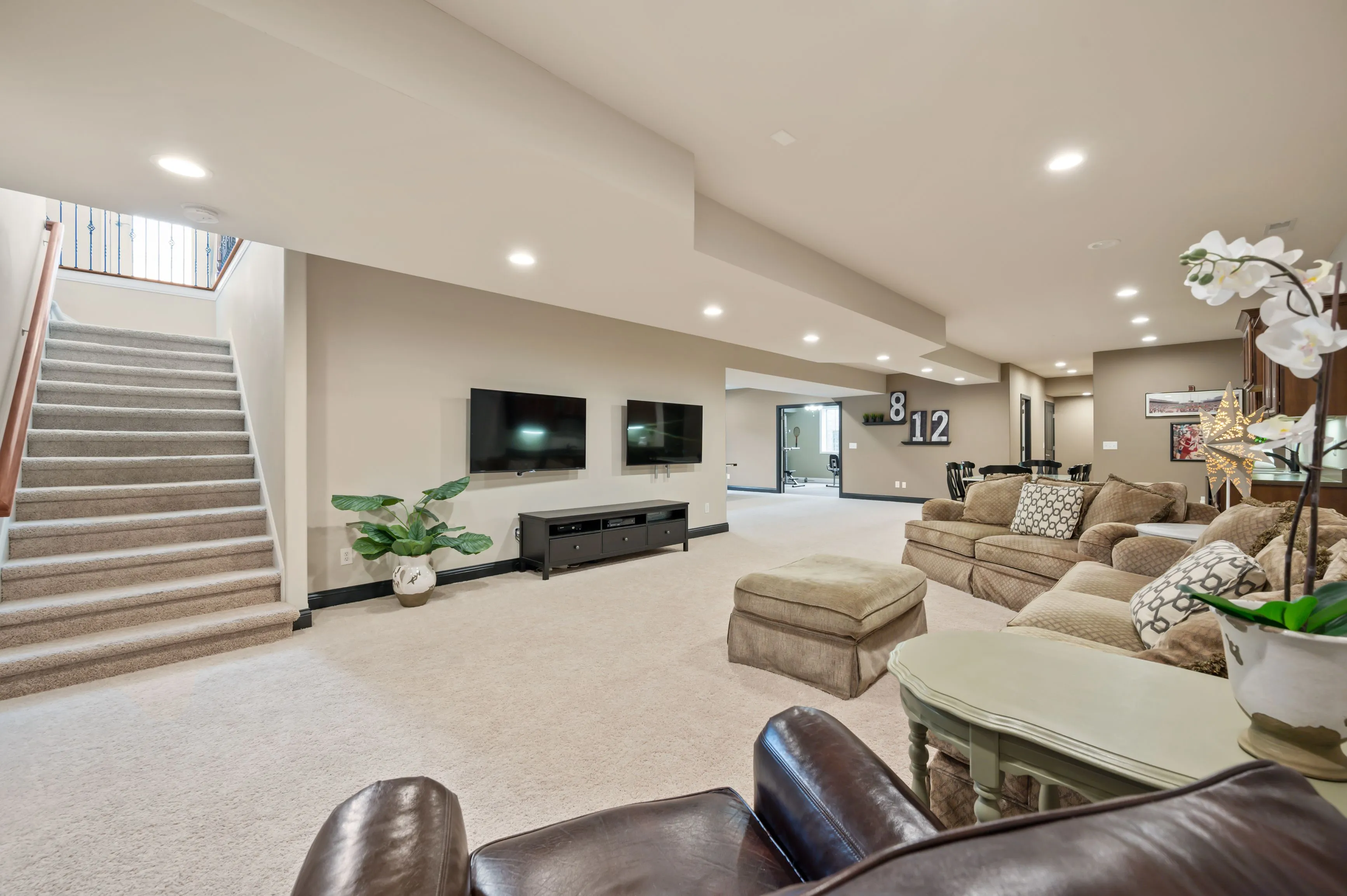 Spacious modern basement living area with sectional sofa, flat-screen TV, and staircase.