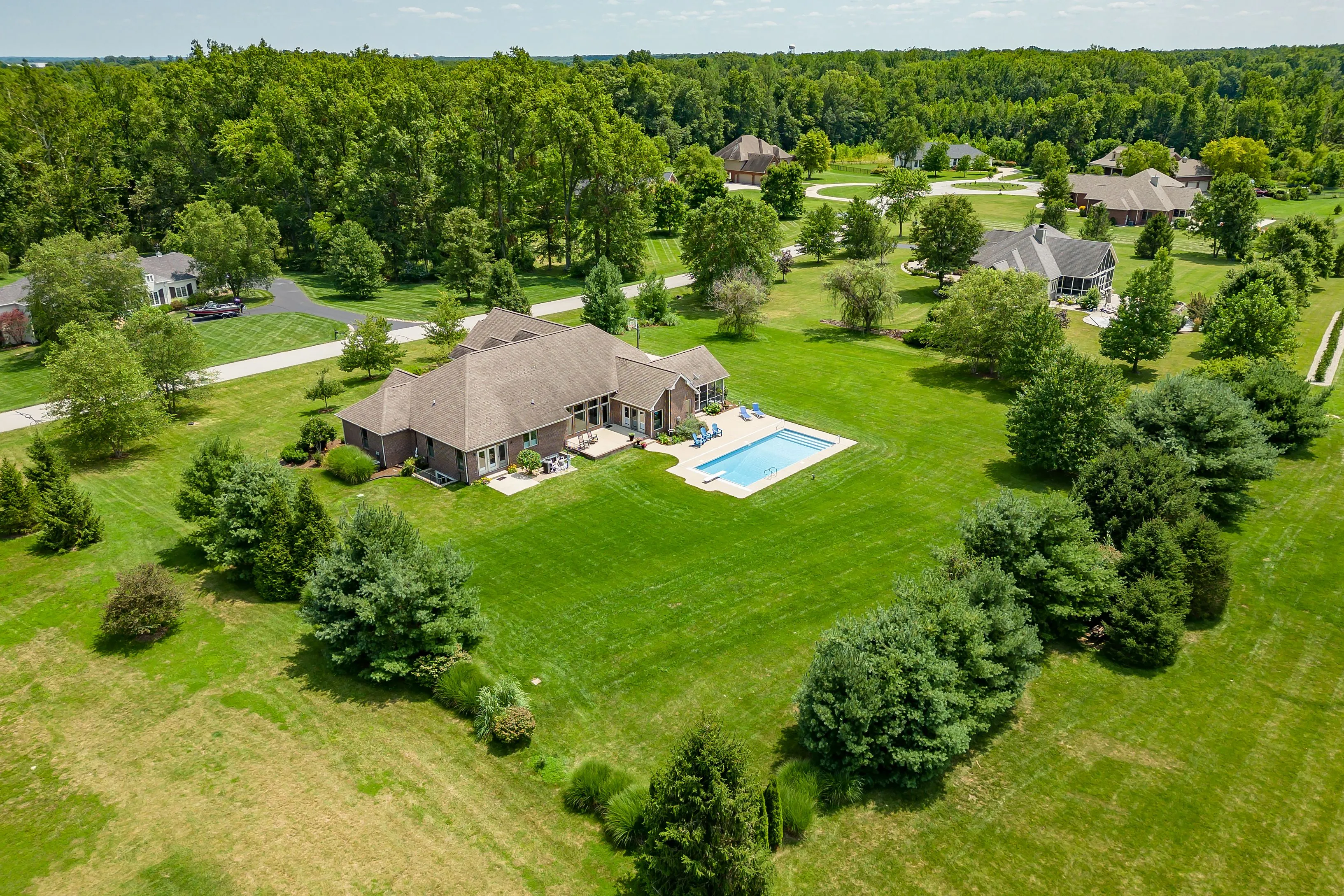 Aerial view of a spacious residential property with a large house, swimming pool, and surrounding greenery.