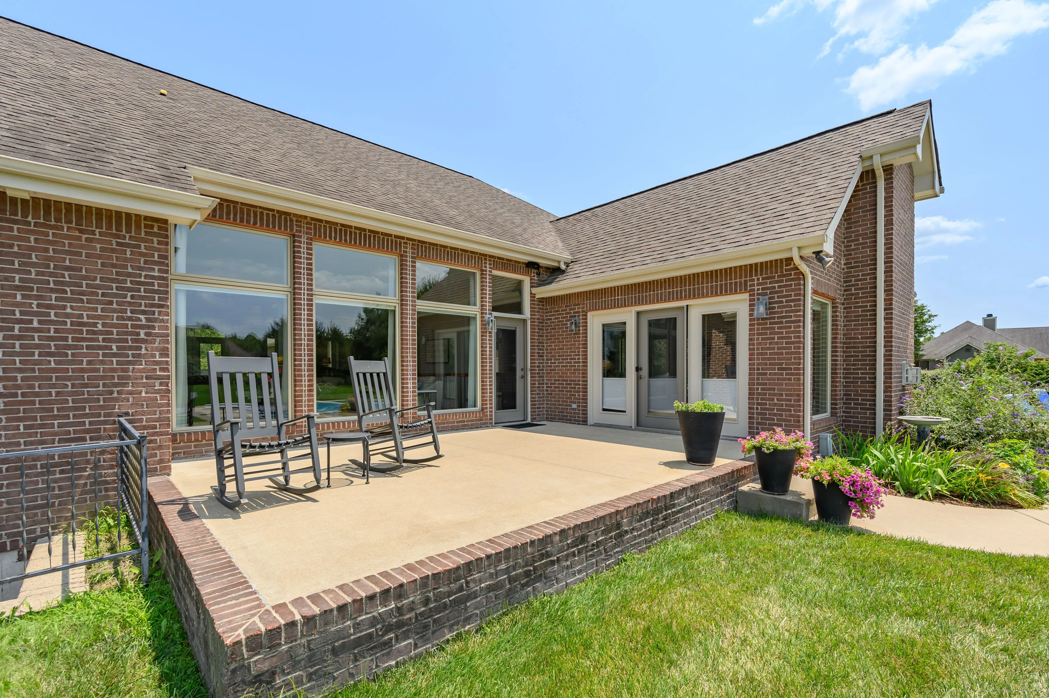 Exterior view of a brick house with large windows and a patio featuring rocking chairs.