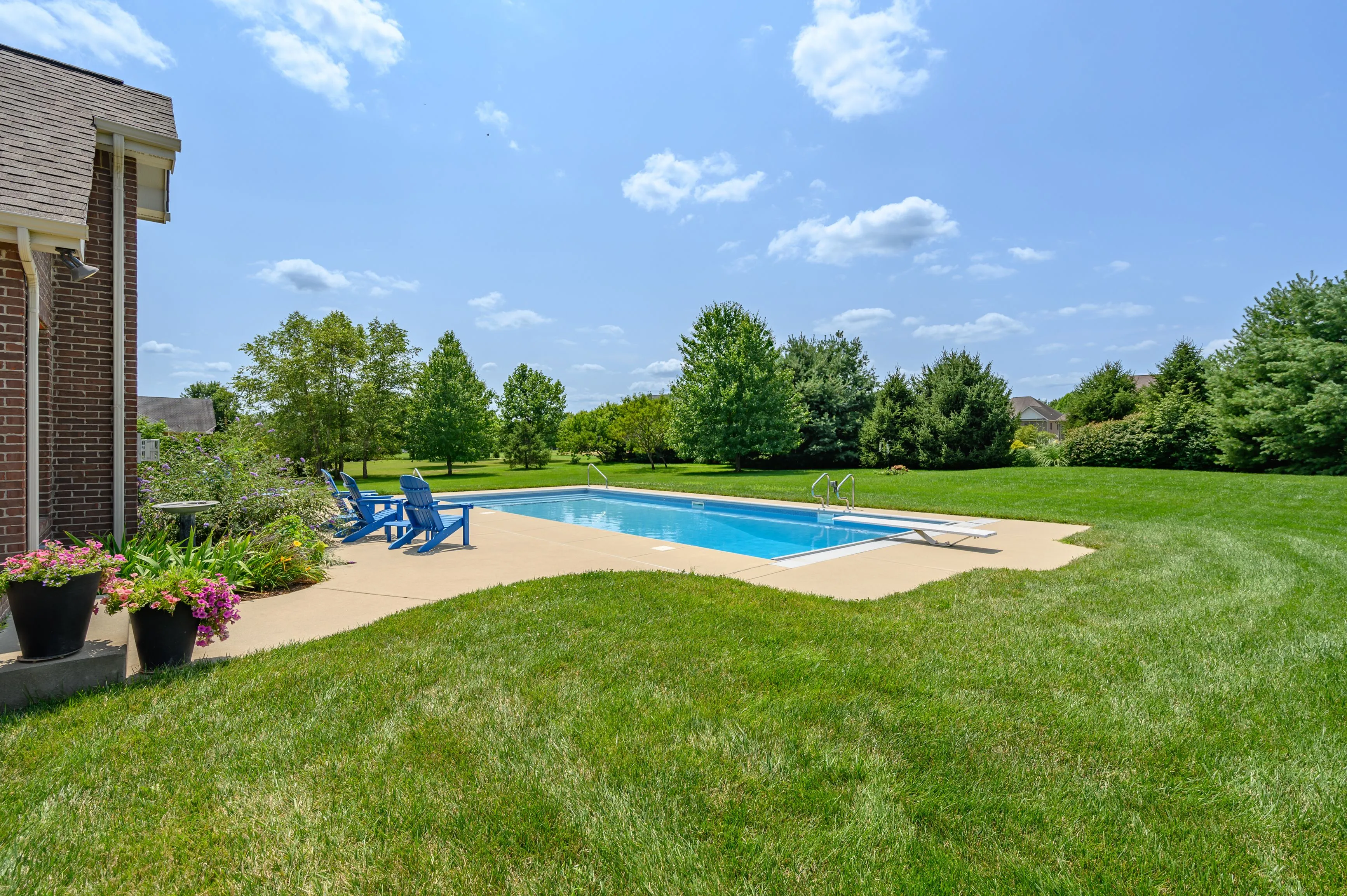 Backyard with a swimming pool, lounge chairs, and surrounding green lawn on a sunny day.