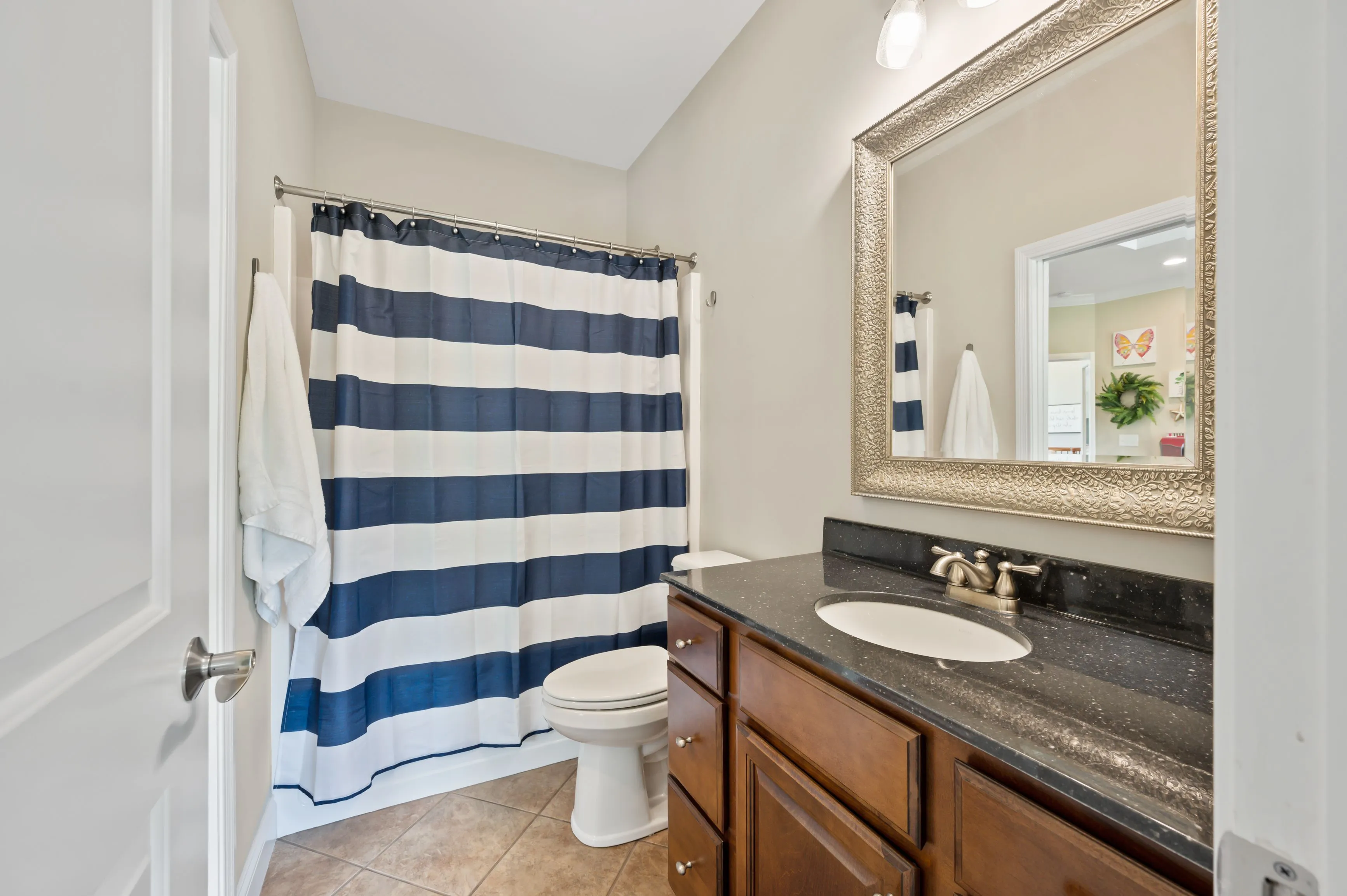 Modern bathroom interior with striped shower curtain, wooden vanity cabinet, and large mirror.