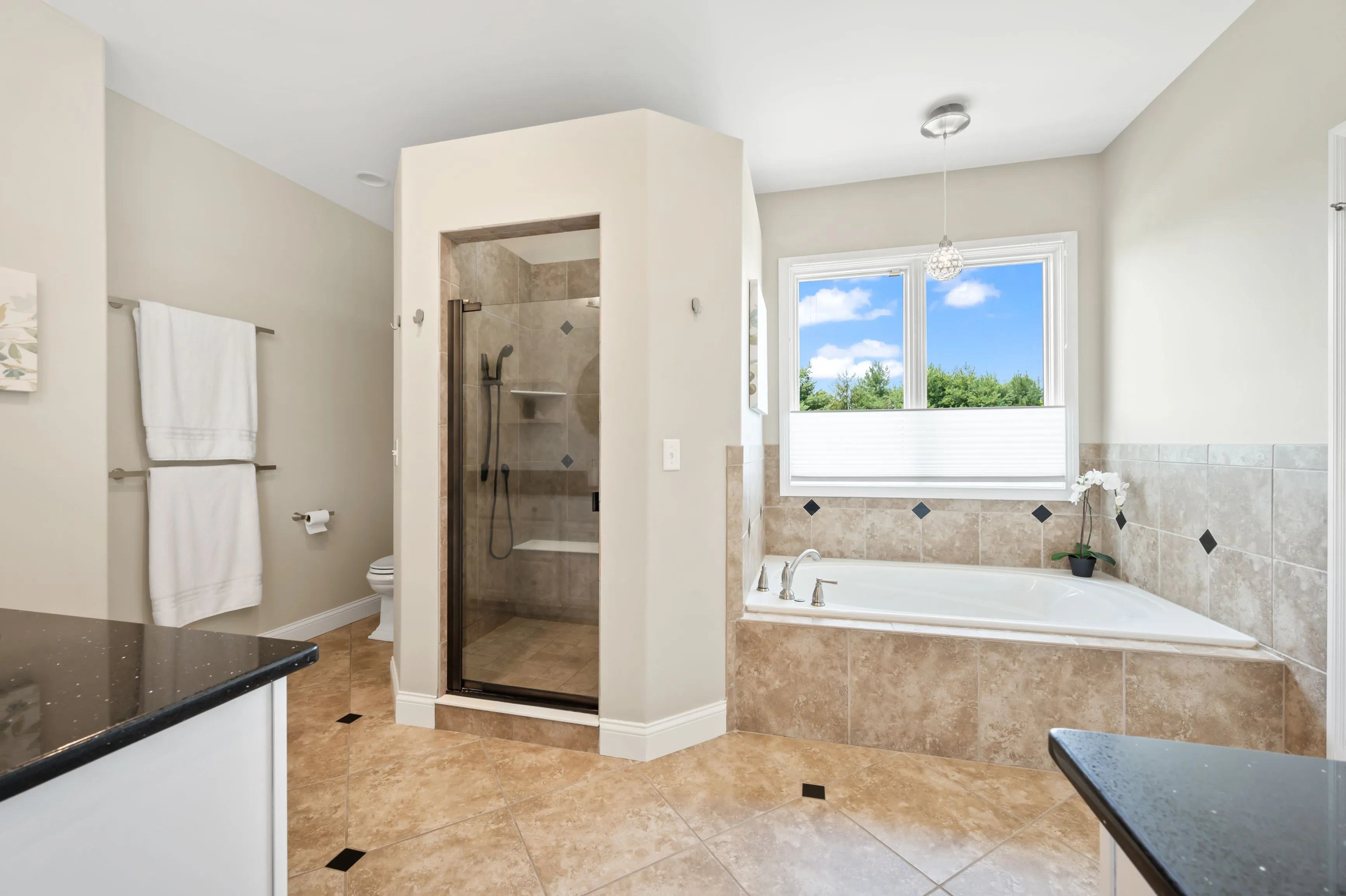 Bright modern bathroom with a shower cabin, bathtub, and a large window showing a sunny day outside.