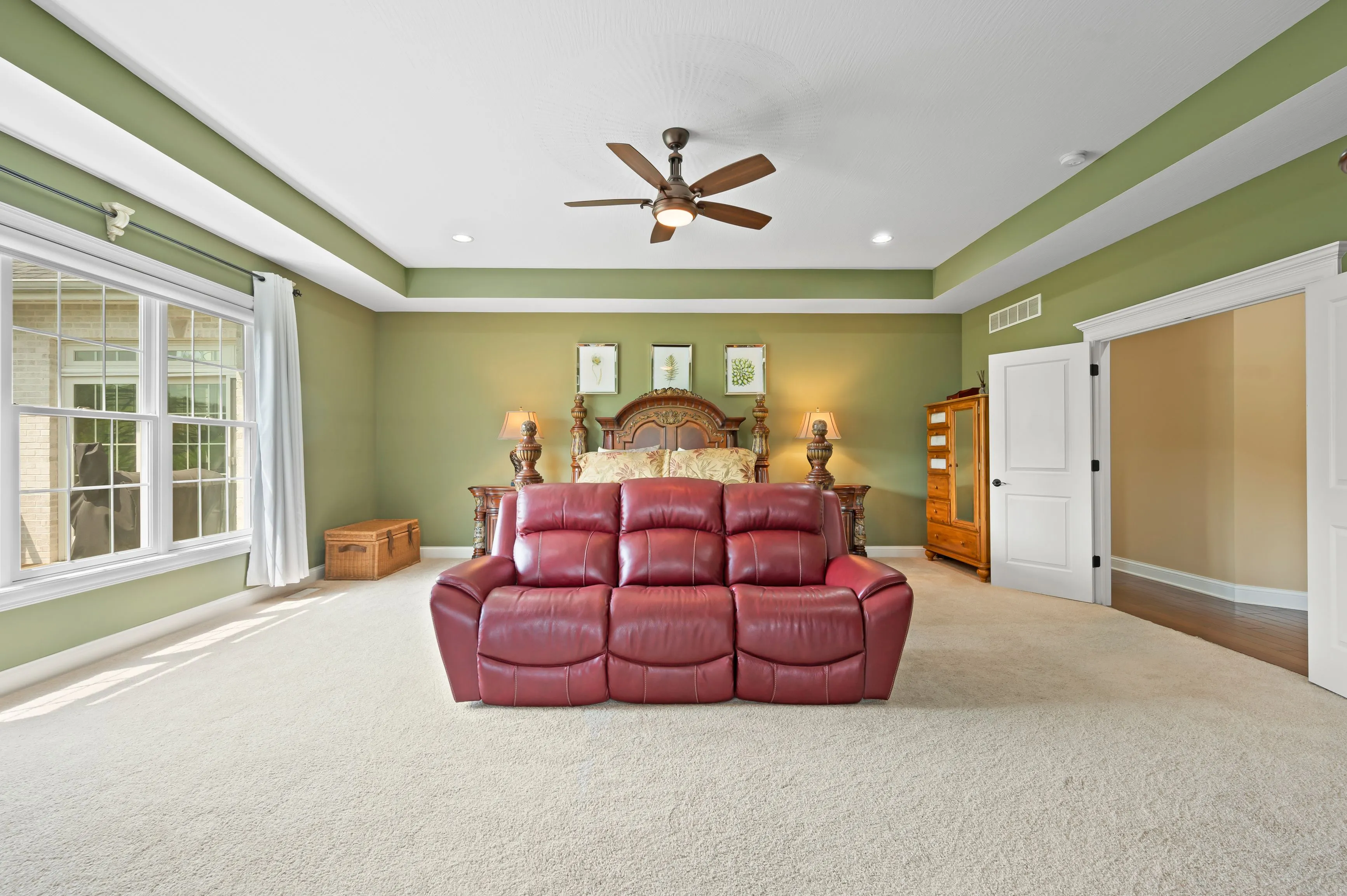 Spacious bedroom with green walls, large red leather sofa, wooden furniture, and a ceiling fan.