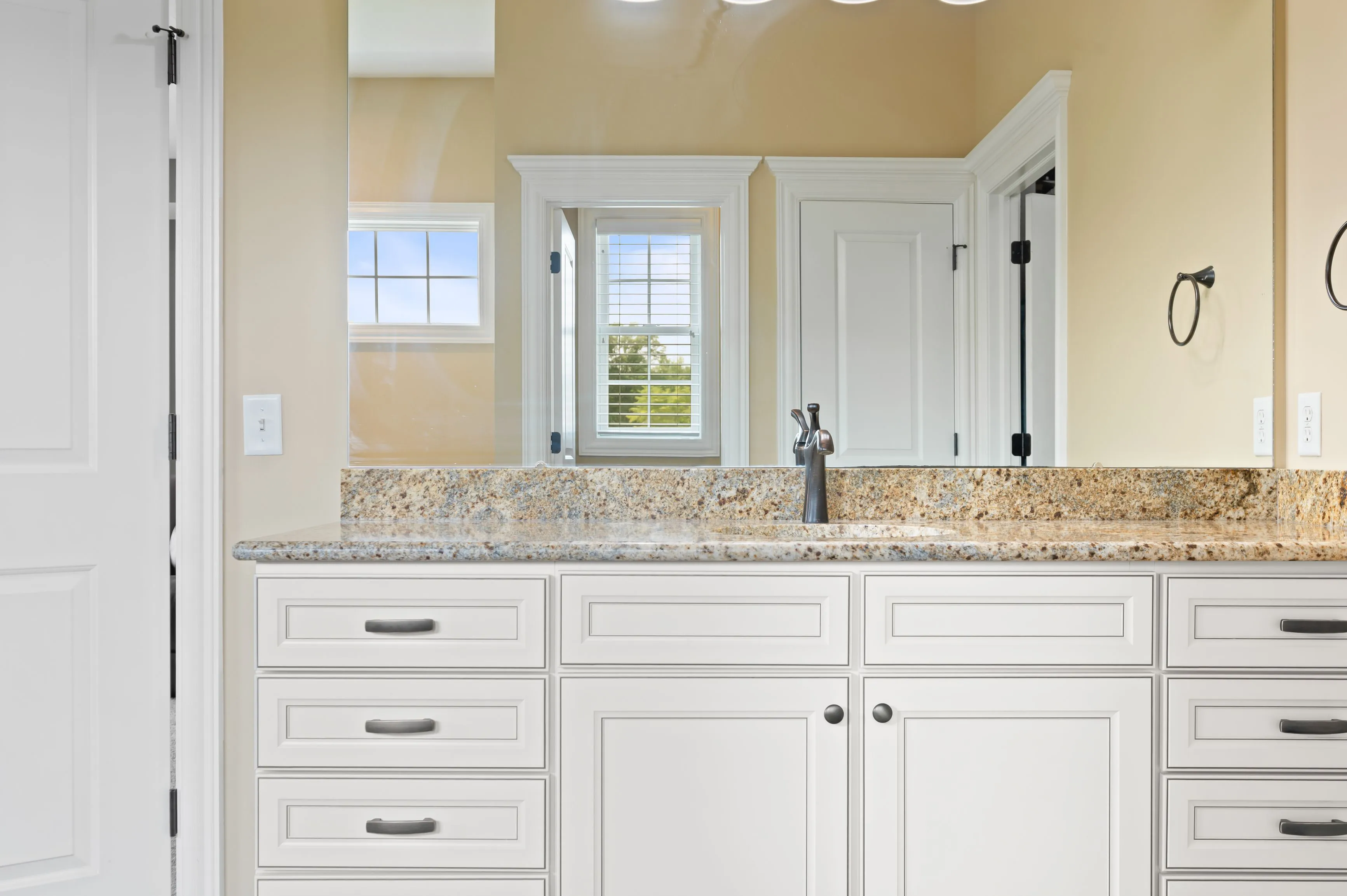 Modern bathroom interior with granite countertop, white cabinets, and a small window.