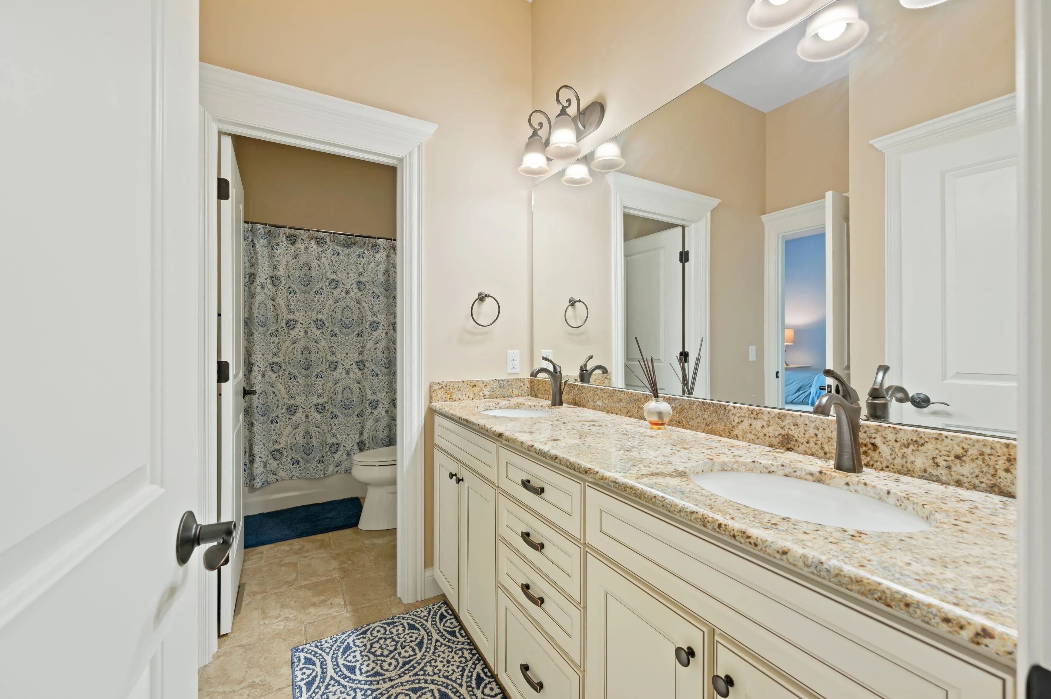 Spacious bathroom interior with double vanity sink, large mirror, and a separate toilet area with a patterned shower curtain.