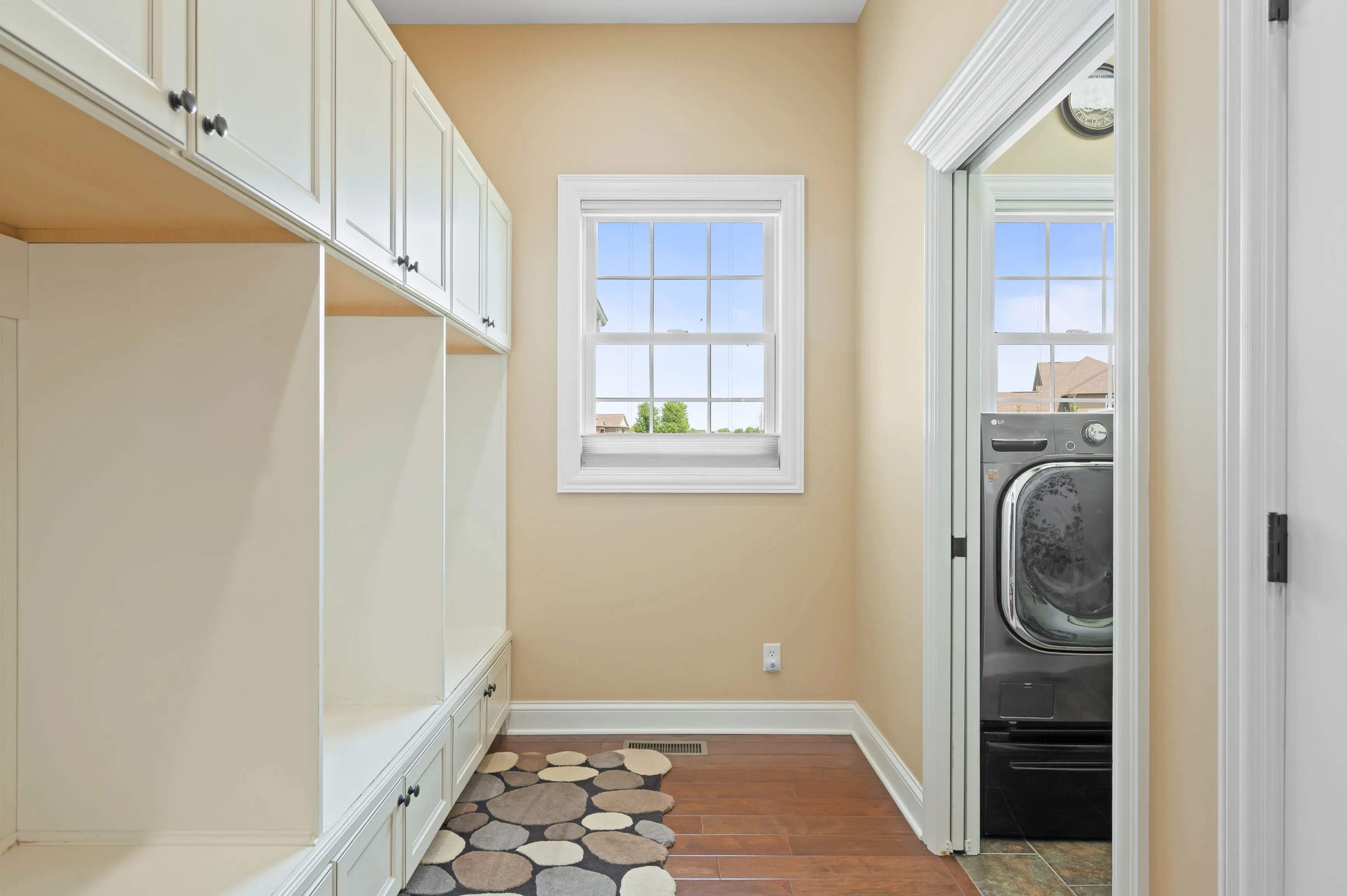 Bright and airy laundry room with built-in cabinets, a window, and modern appliances.