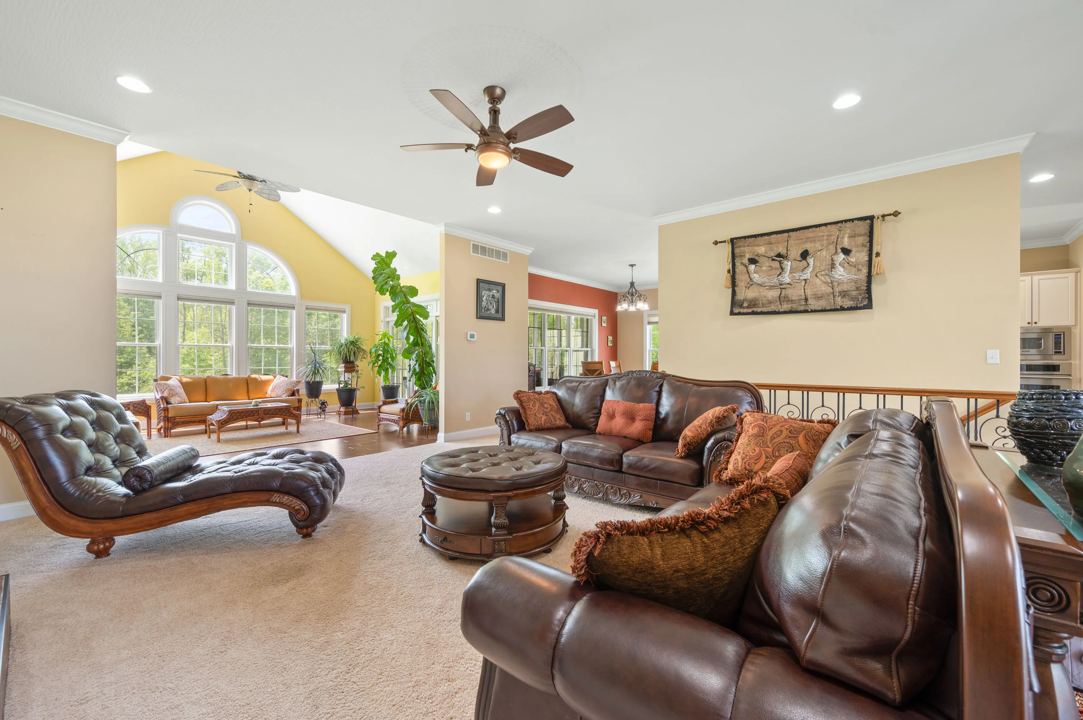 Spacious living room with high ceilings, large arched windows, tan walls, and leather furniture.