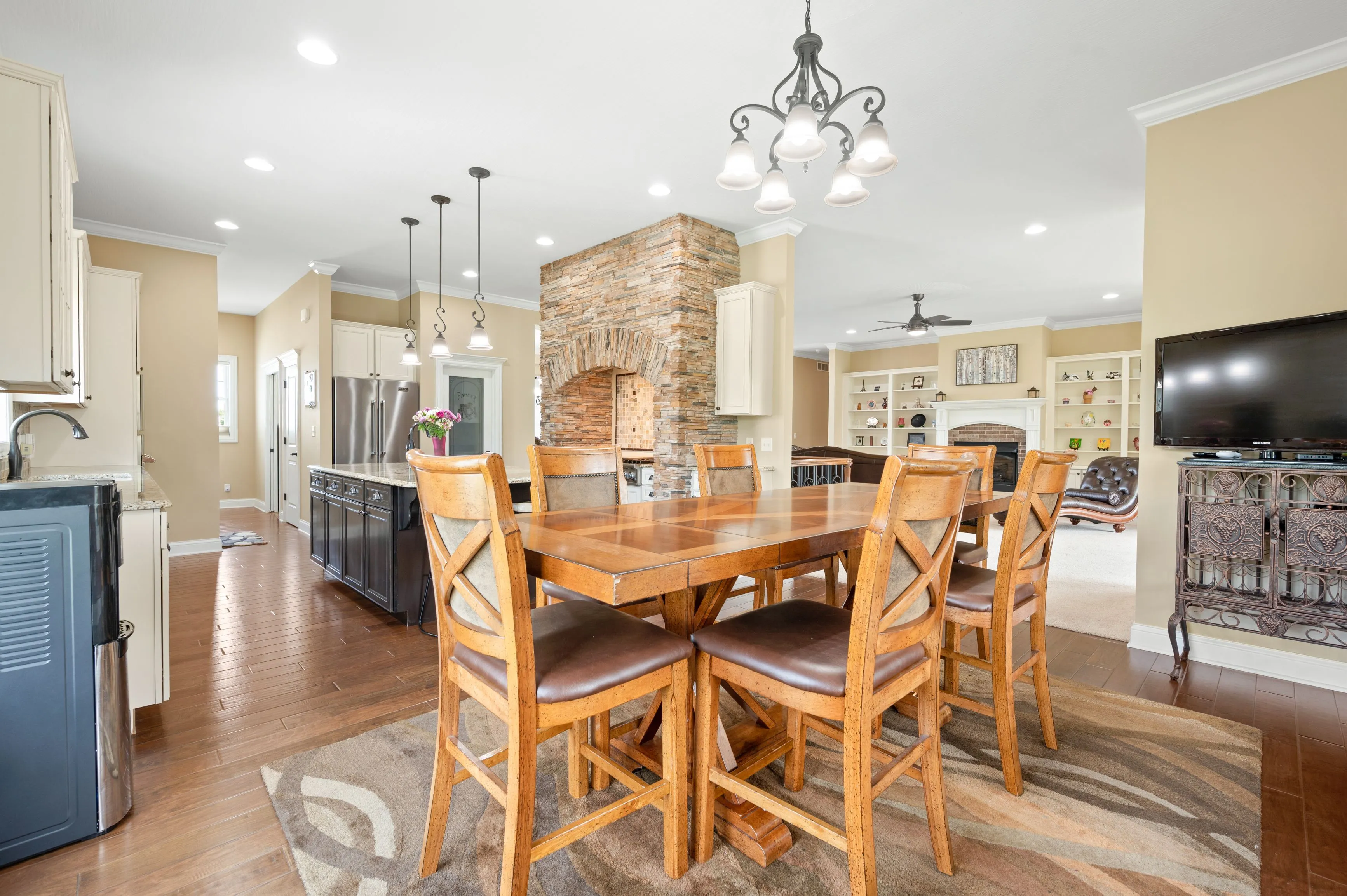 Spacious dining area with a large wooden table, leather chairs, hardwood floors, a stone fireplace, and an open kitchen with stainless steel appliances.