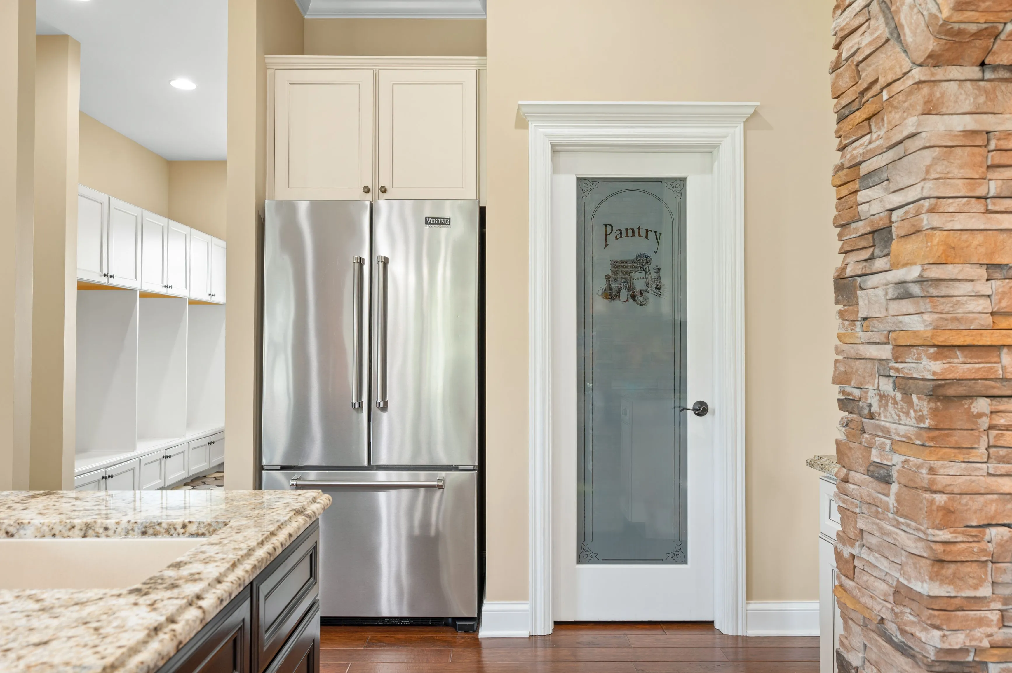 Modern kitchen interior with stainless steel refrigerator next to a white pantry door and stone column.