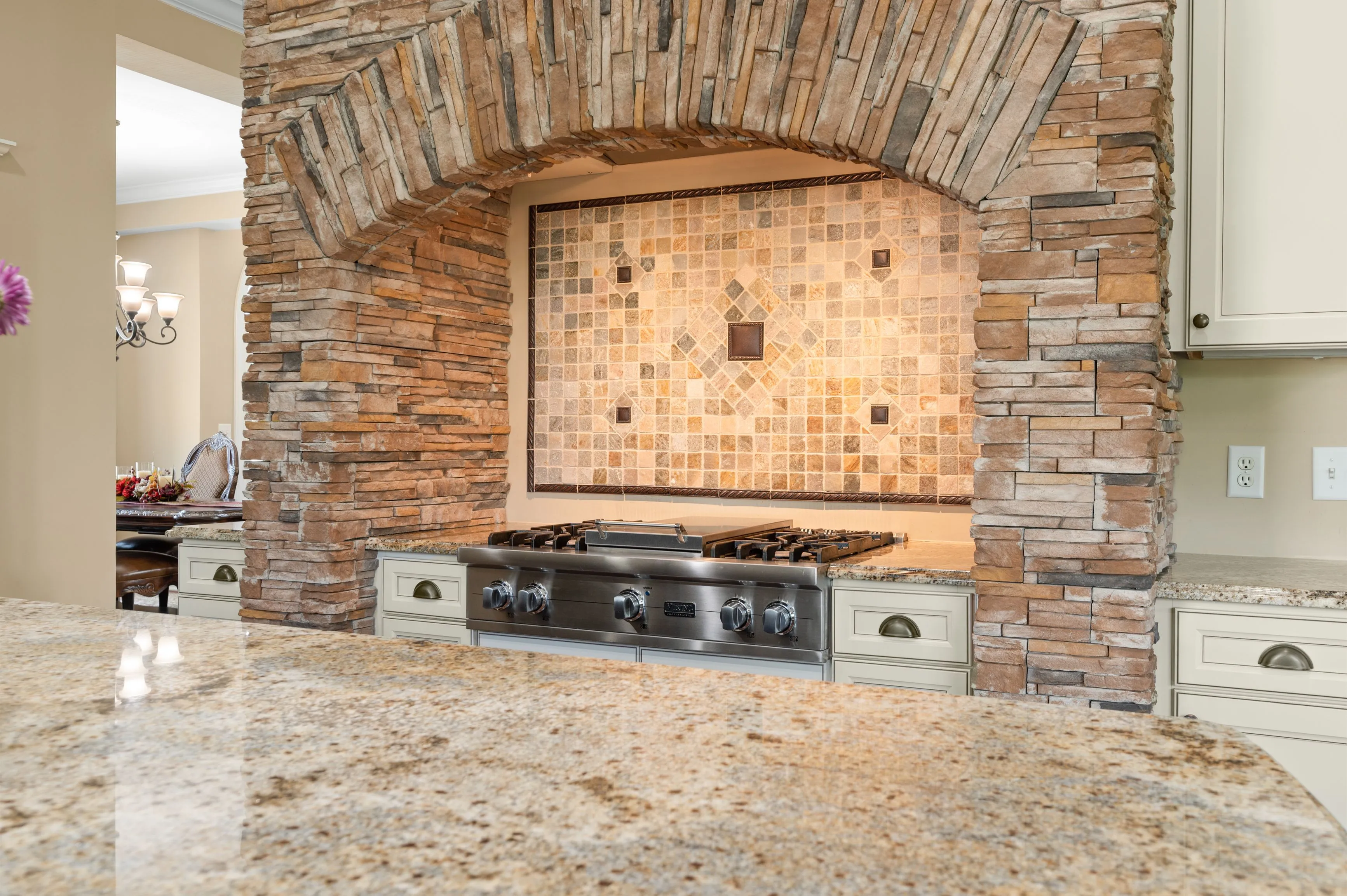 Modern kitchen with stone archway over a stainless steel gas stove and decorative tile backsplash.