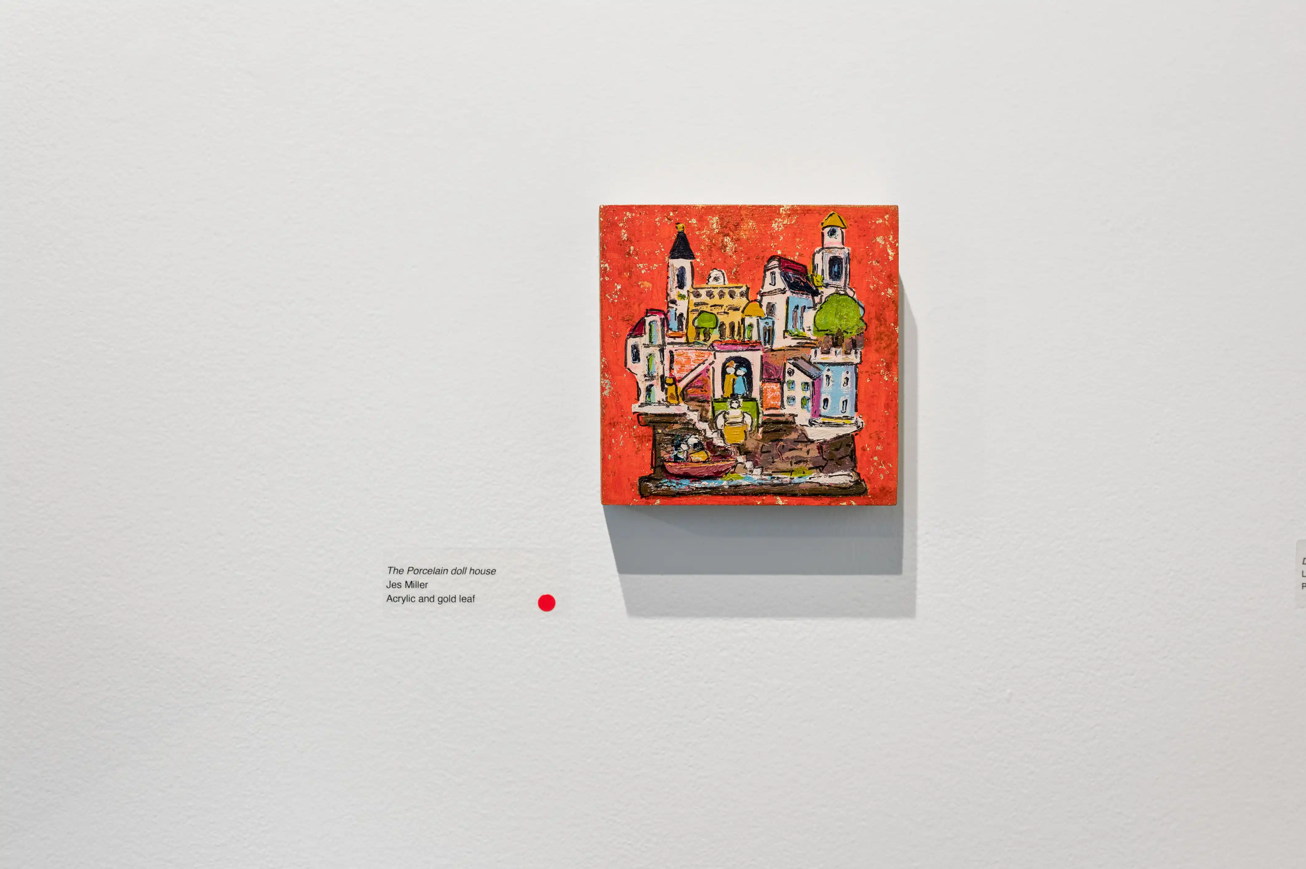 Colorful painting displayed on a white gallery wall with a small description card to the left side; red dot sticker indicating sale status below.