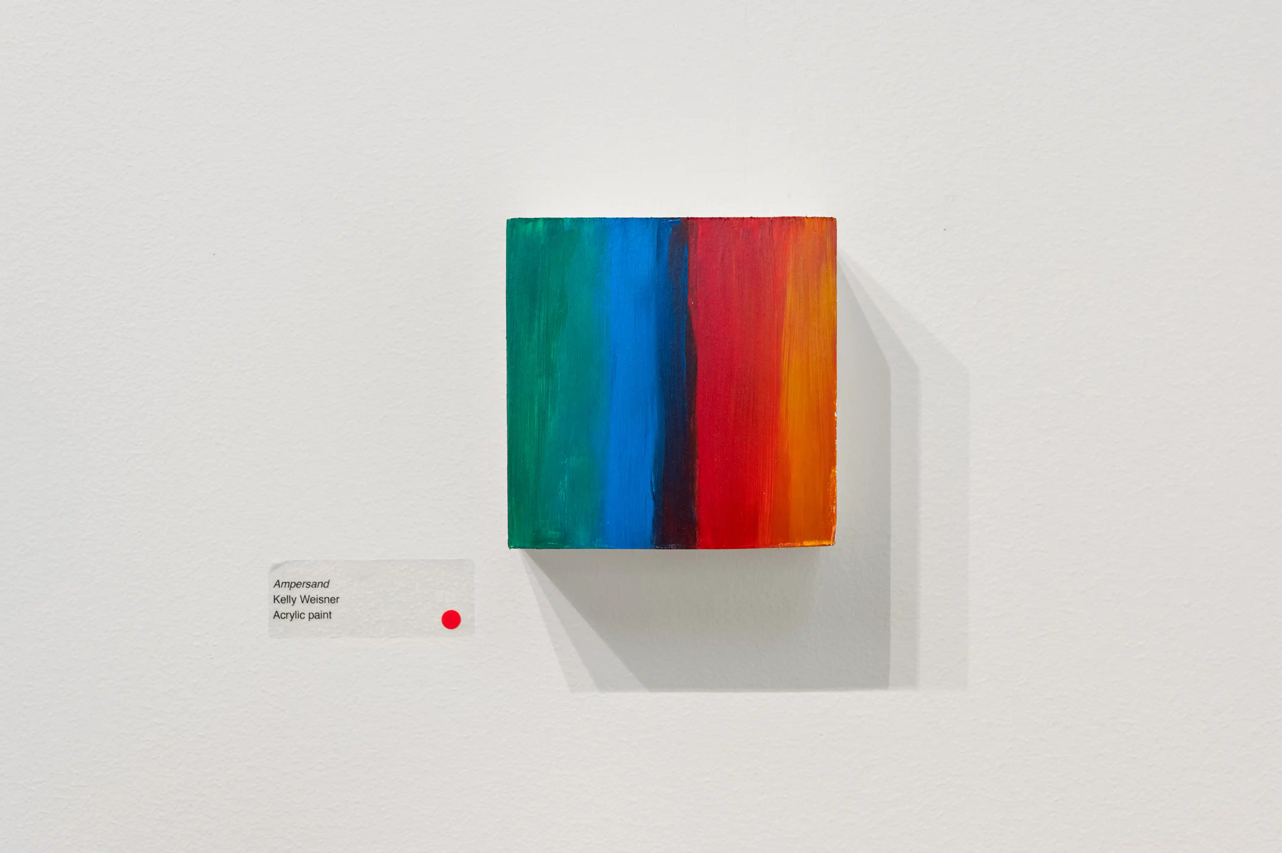 Modern art canvas with vibrant vertical stripes in red, blue, and green, displayed on a white gallery wall with description plaque.