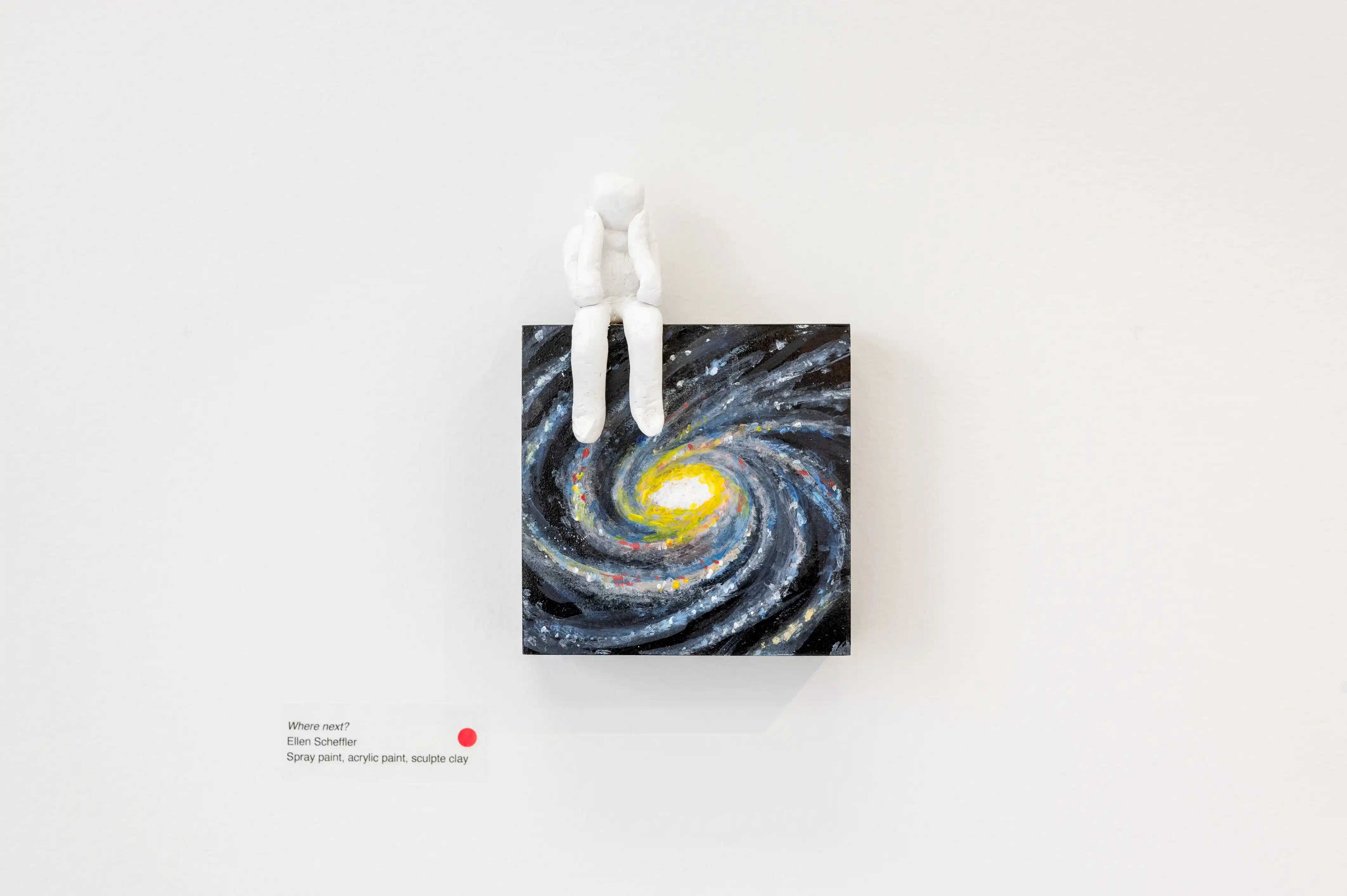 A minimalist art piece featuring a 3D figure seated on top of a canvas painted with a swirling galaxy, hanging on a white wall.