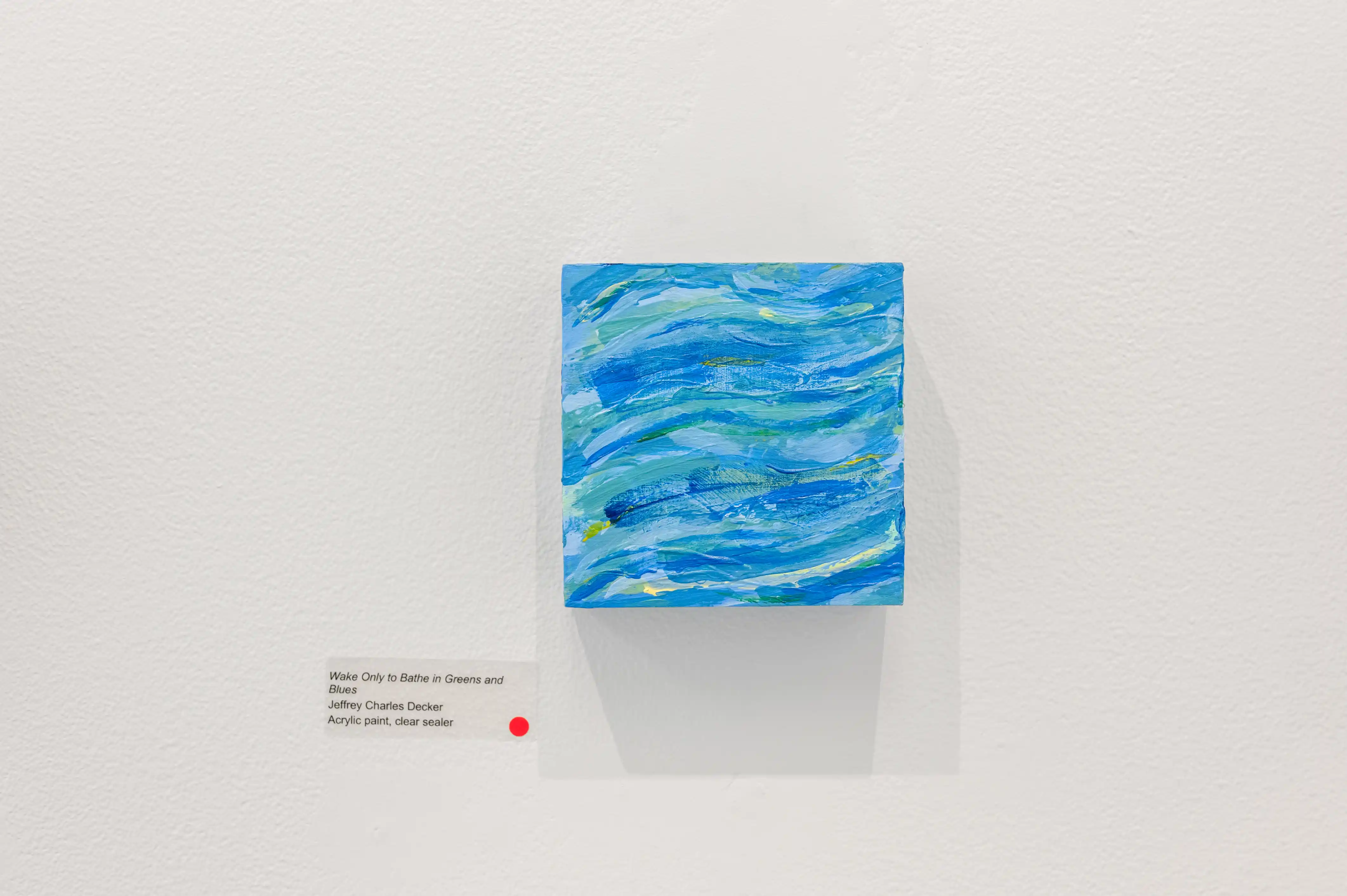 "Abstract blue ocean waves painting on a white gallery wall with a small informational plaque and red dot indicating the artwork is sold"