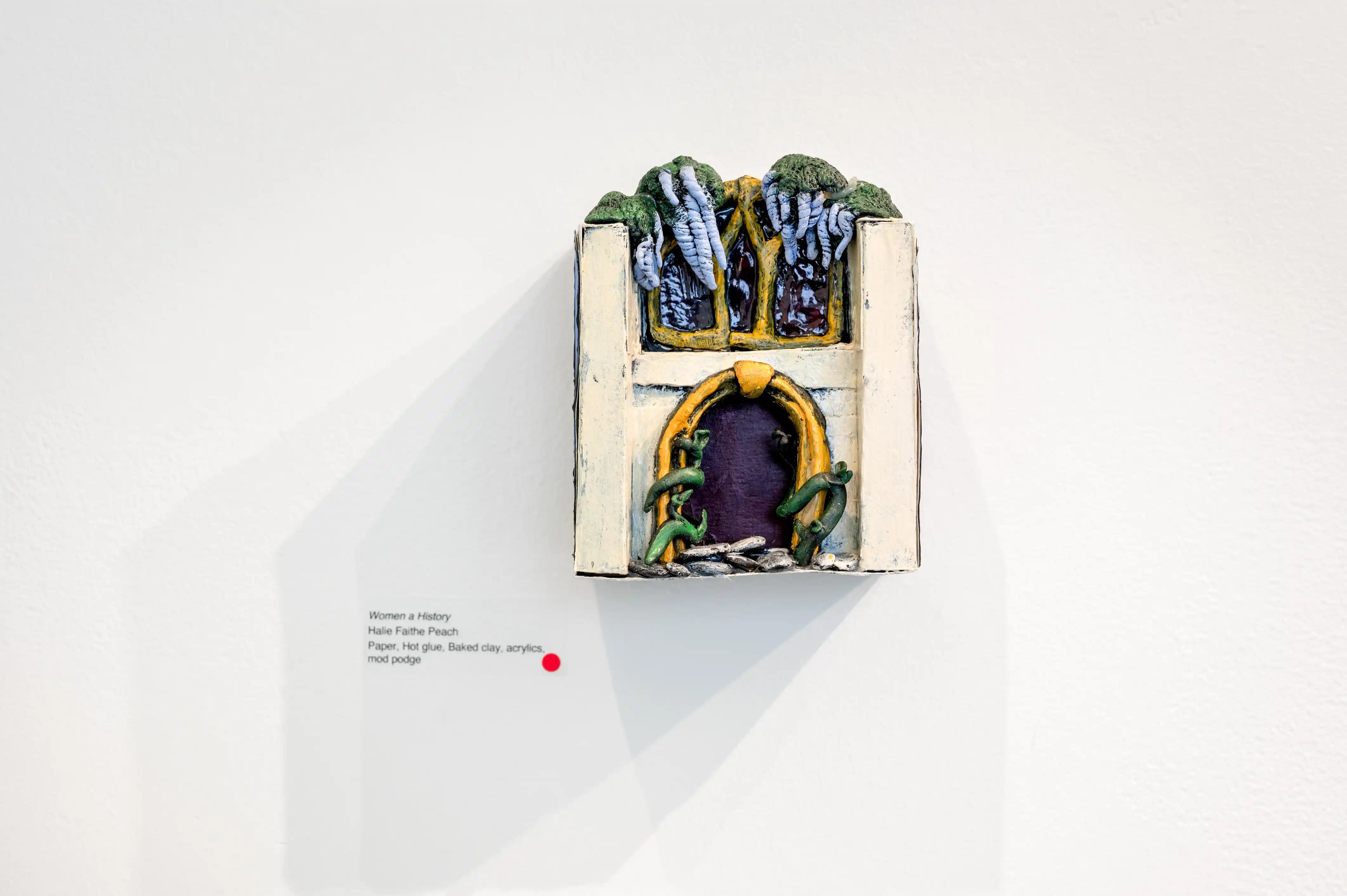 3D miniature sculpture of a medieval church facade displayed on a gallery wall with an informational plaque beside it.