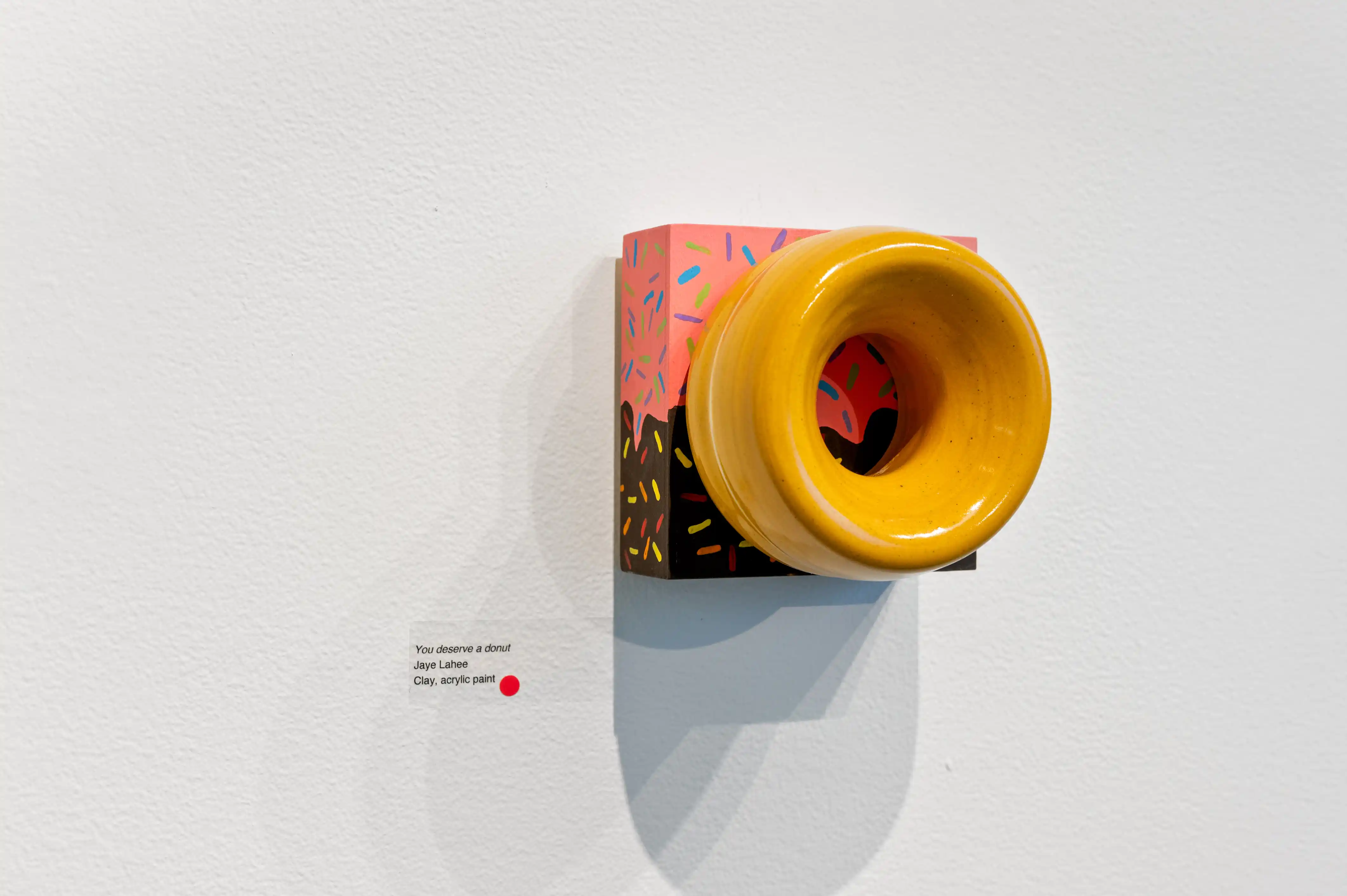 Art installation featuring a yellow megaphone emerging from an opening in a colorful abstract-patterned book on a white wall.