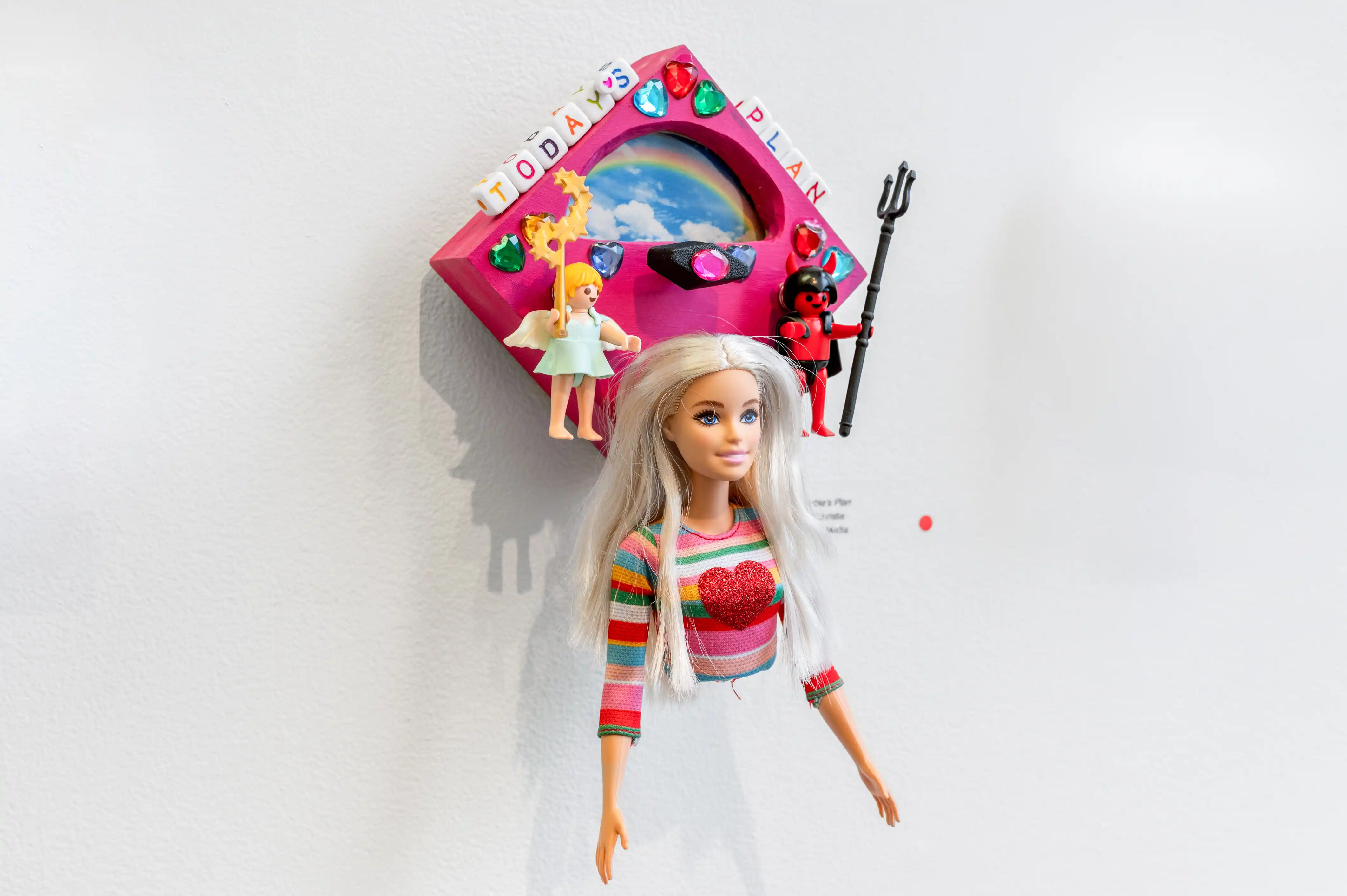 Barbie doll attached to a wall below a colorful dollhouse shelf with accessories.