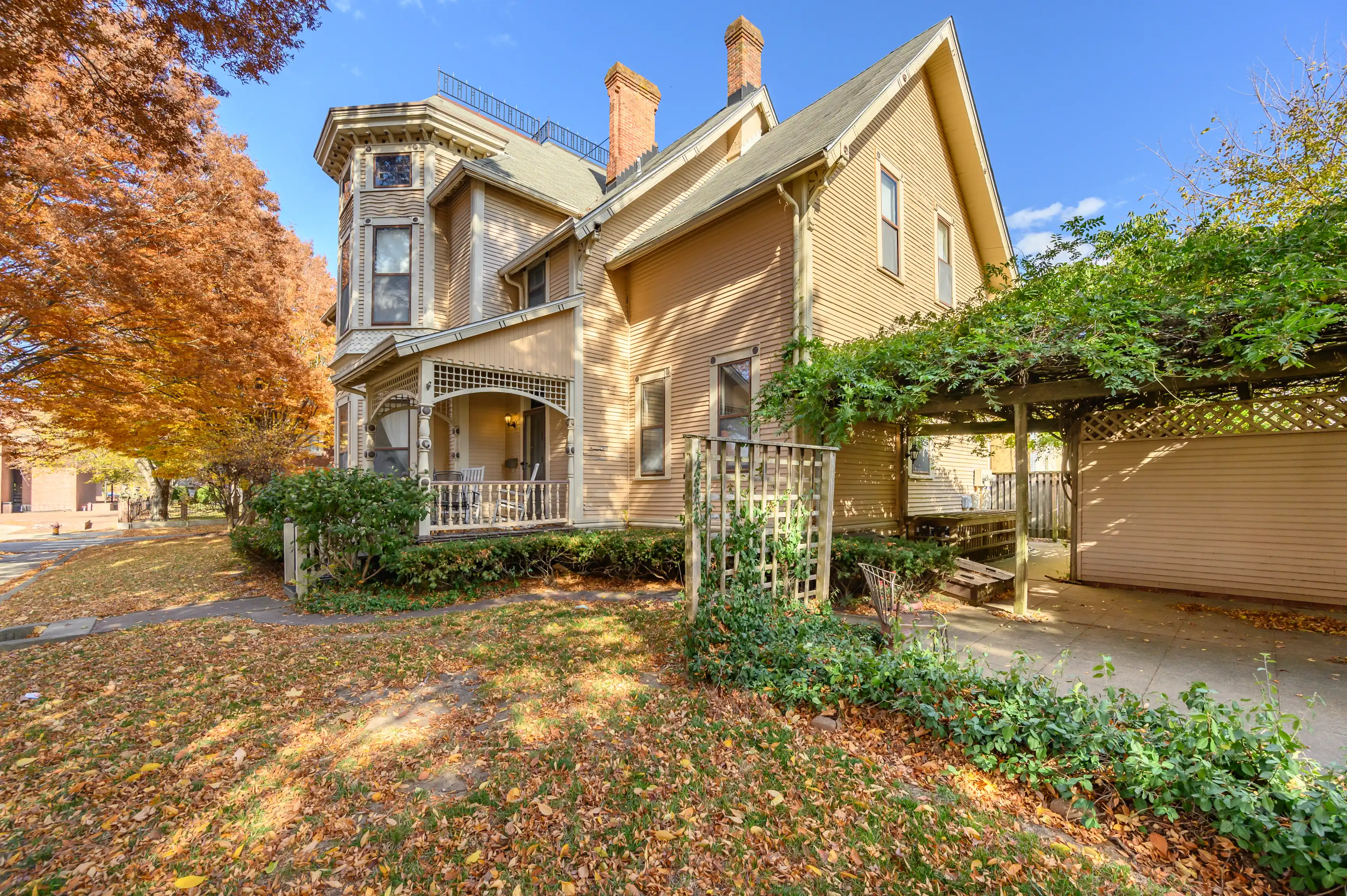 Victorian-style house with a covered porch and a carport surrounded by fallen autumn leaves.