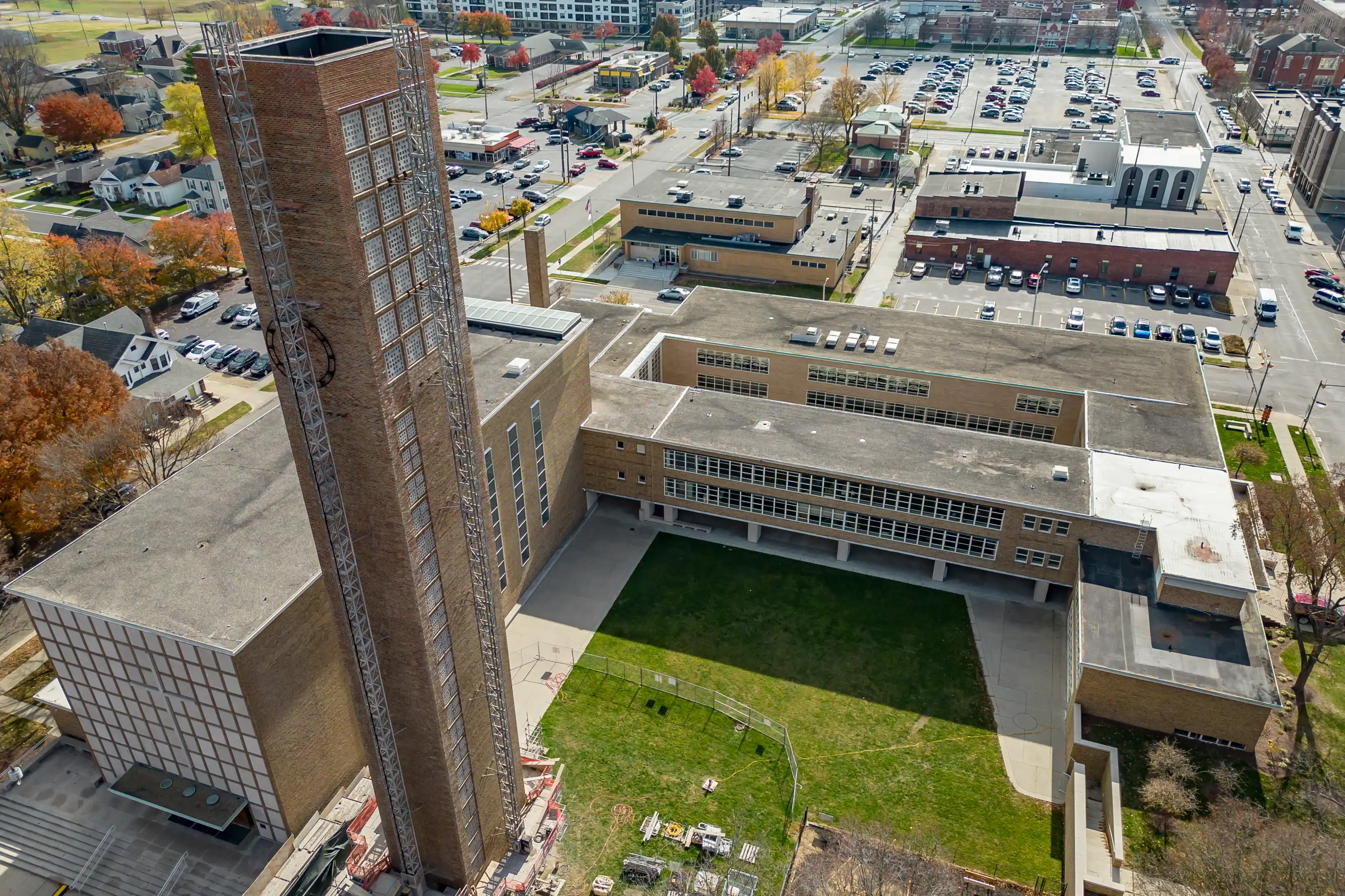 Aerial view of a tall brick chimney attached to a large building with adjacent parking lots and surrounding streets in an urban area.