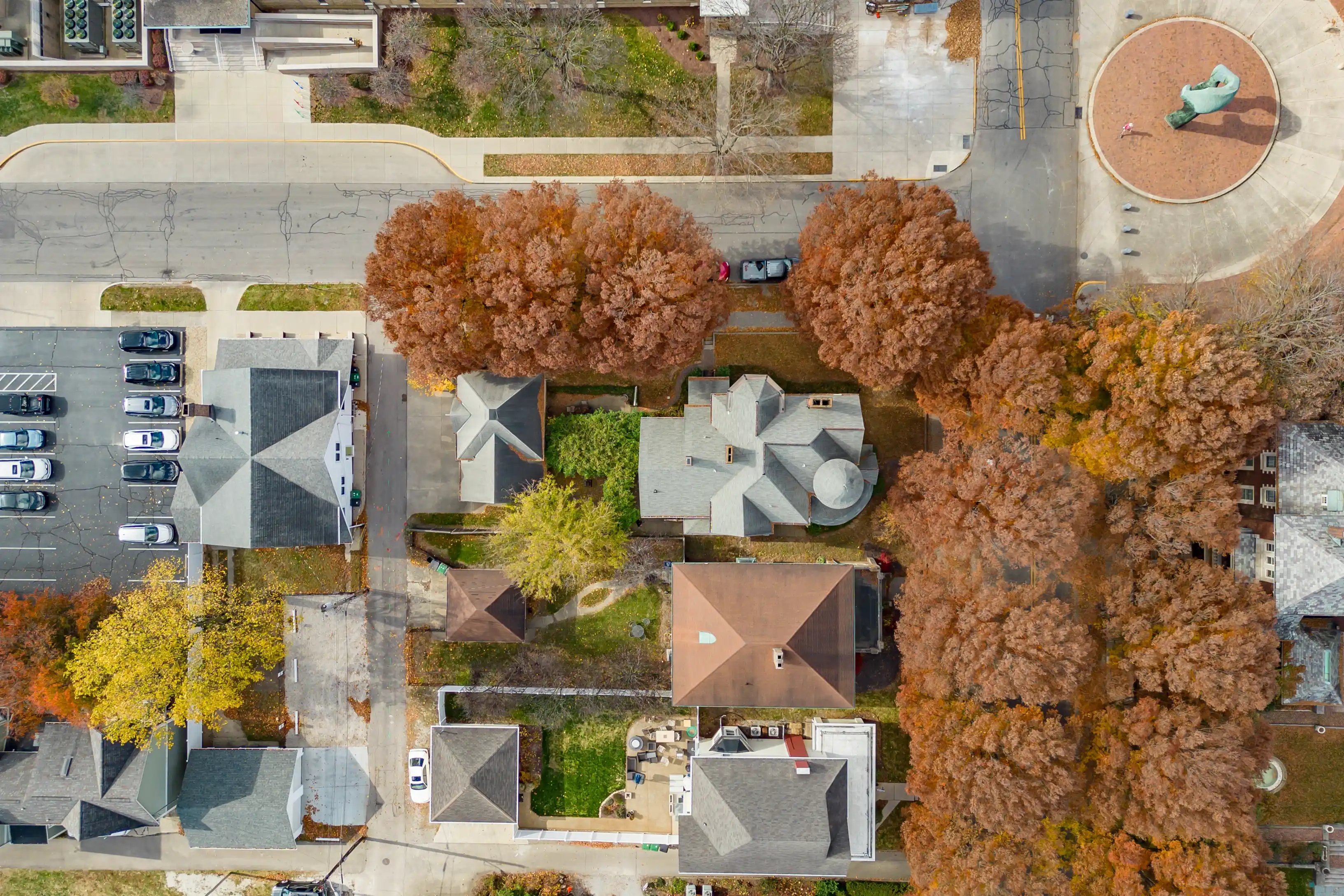 Aerial view of a residential area in autumn with colorful trees, distinctive rooftops, and parked cars.