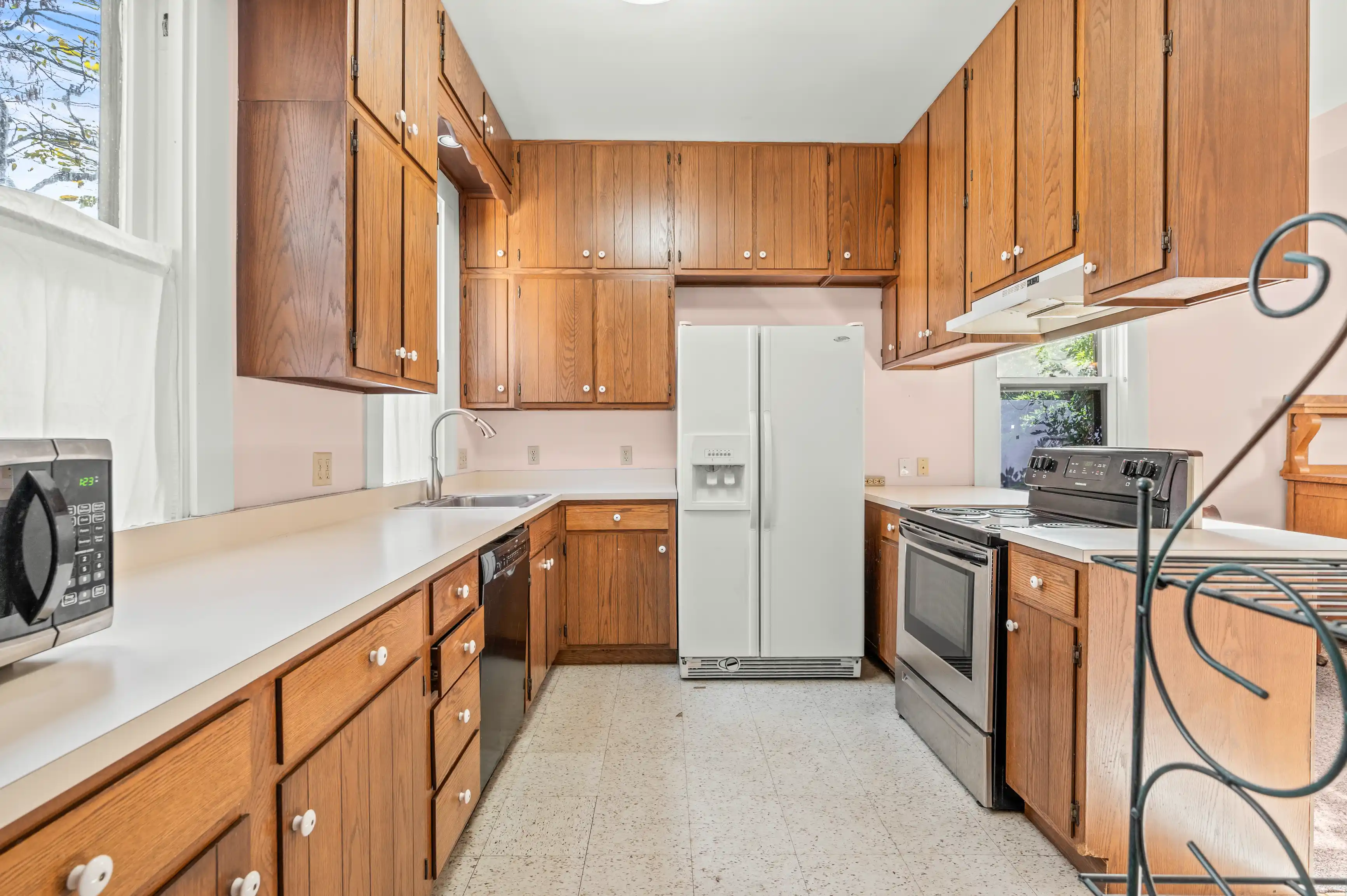 Bright kitchen interior with wooden cabinets, white appliances, and linoleum flooring.