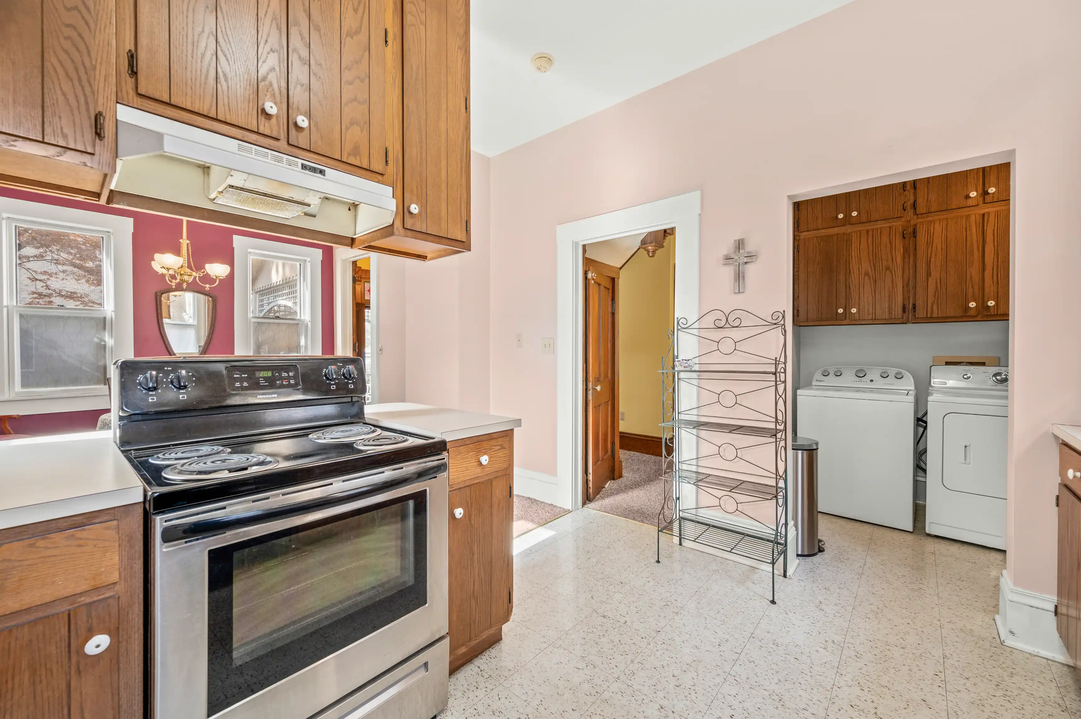 Bright kitchen interior with wooden cabinets, white appliances, and pink walls, featuring a stove, microwave, washer, and dryer.