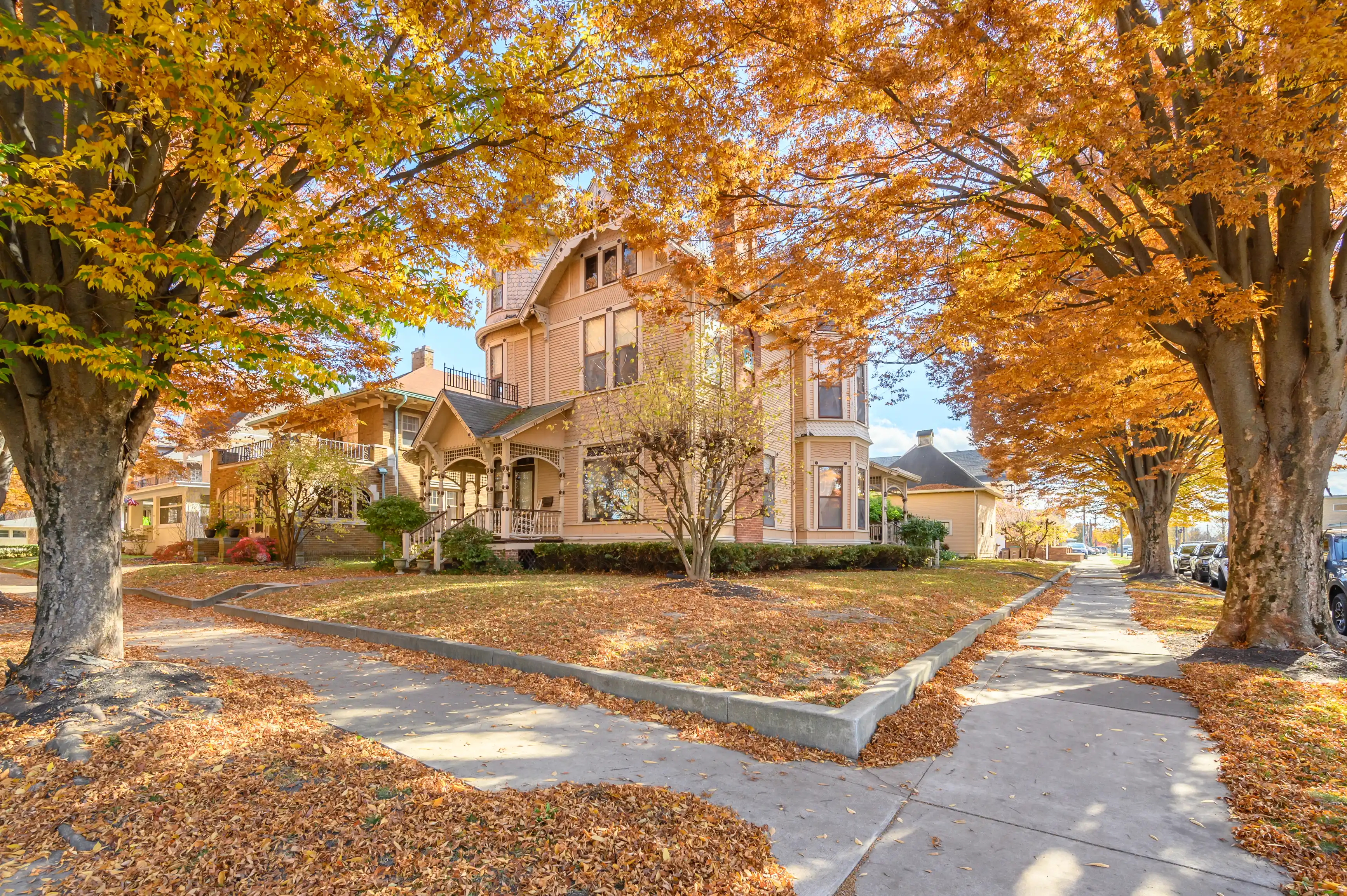 Victorian-style house with a gabled roof surrounded by autumn-colored trees on a sunny day.