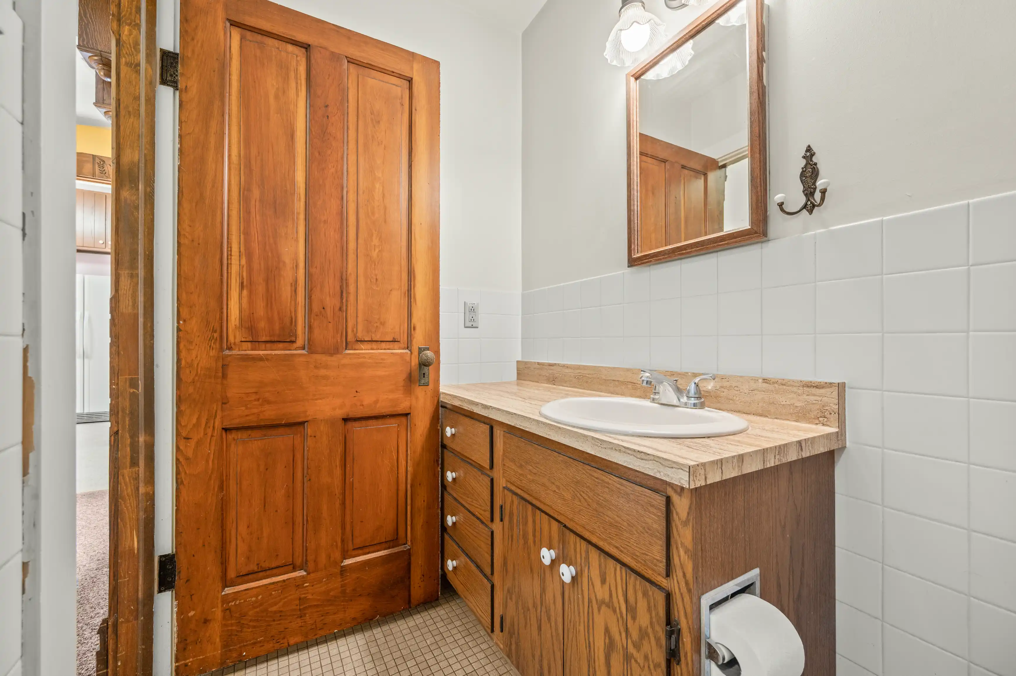 Bright bathroom interior with wooden vanity cabinet, white basin, mirror, and open wooden door leading to another room.