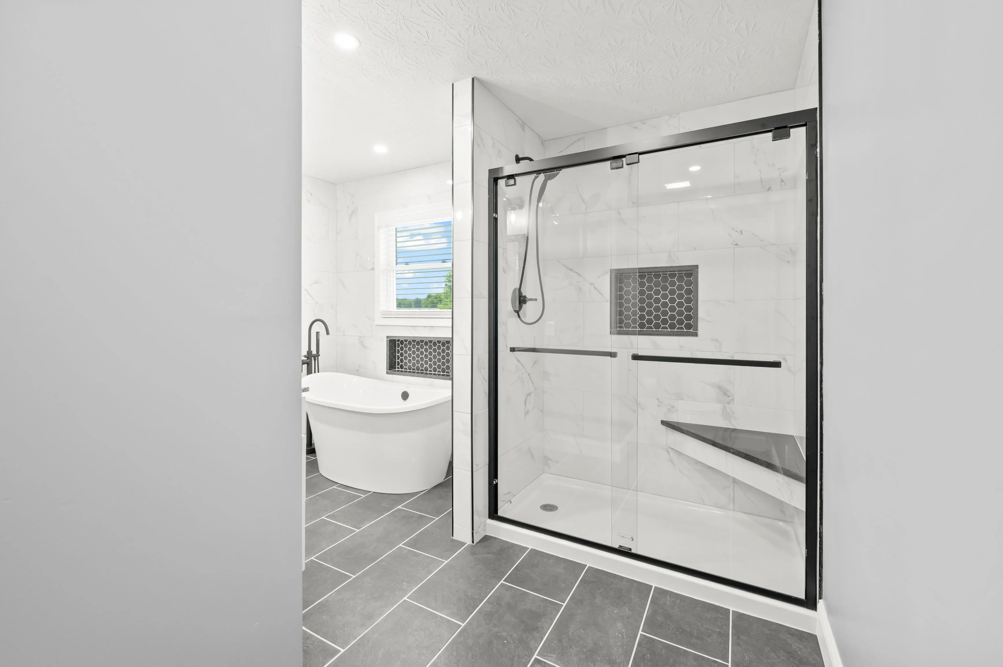 Modern bathroom interior with a freestanding tub, walk-in shower with glass doors, and a window allowing natural light.
