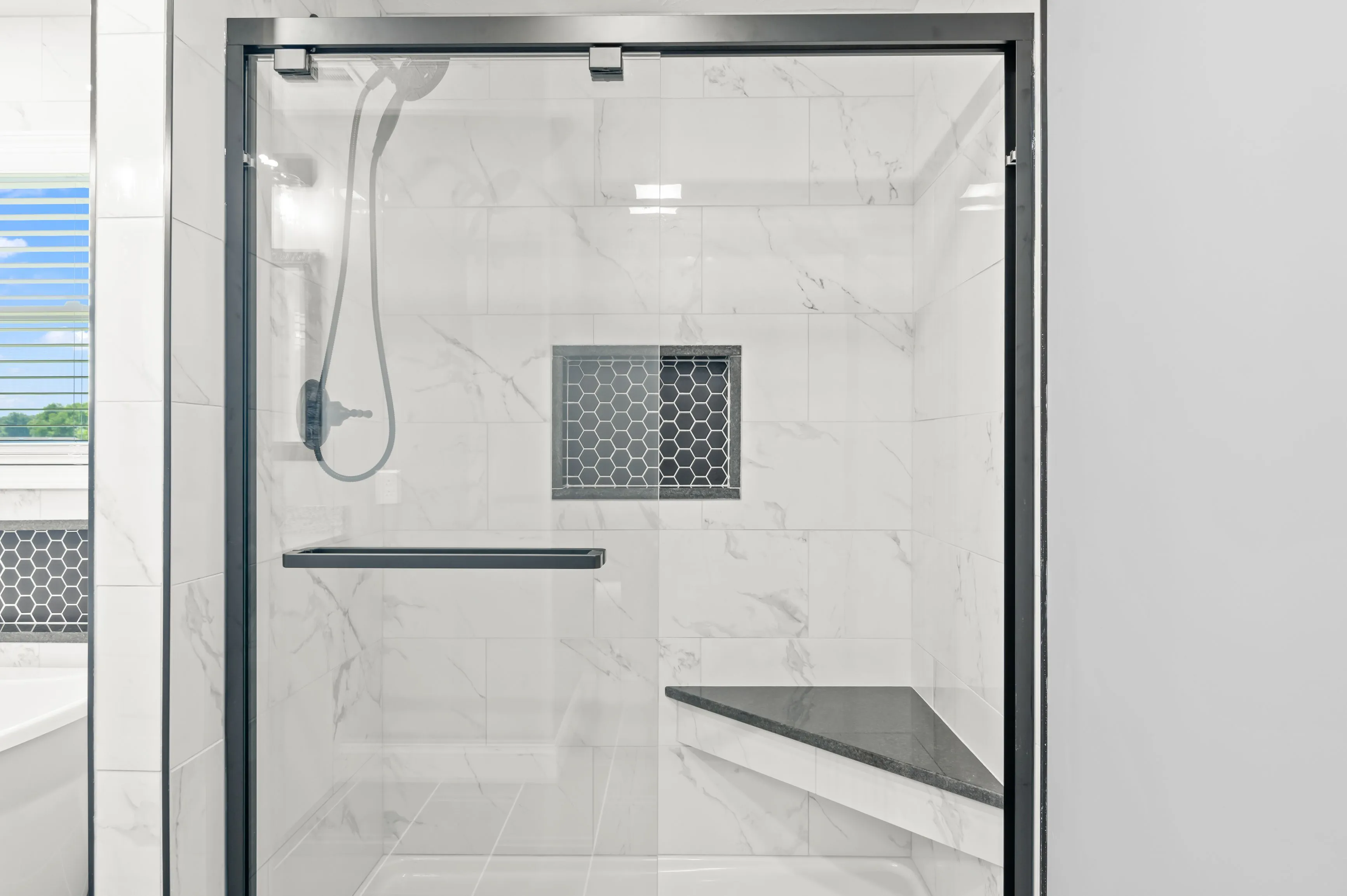 Modern bathroom with marble tiles featuring a glass door shower, built-in wall shelf, and a geometric design window.