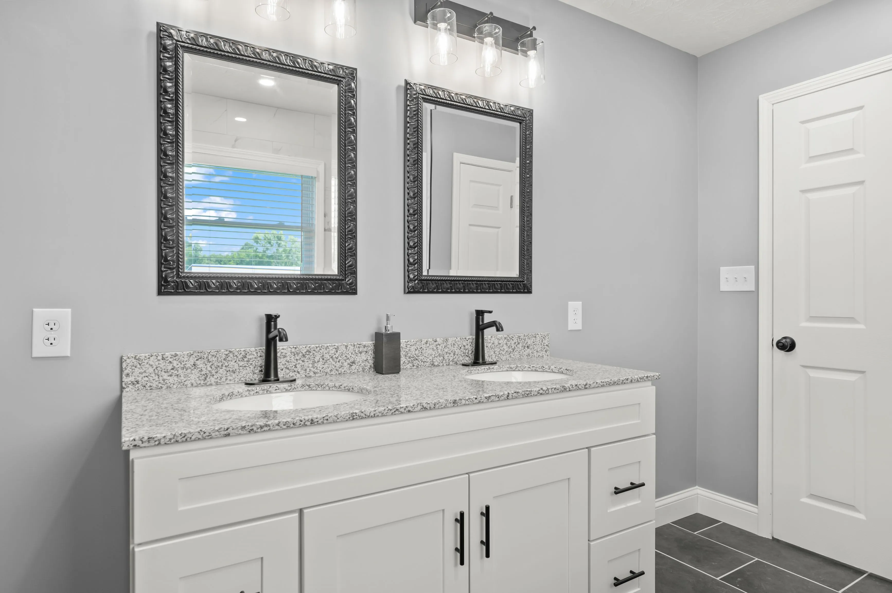 Modern bathroom interior with double sink vanity, large mirrors, and gray walls.