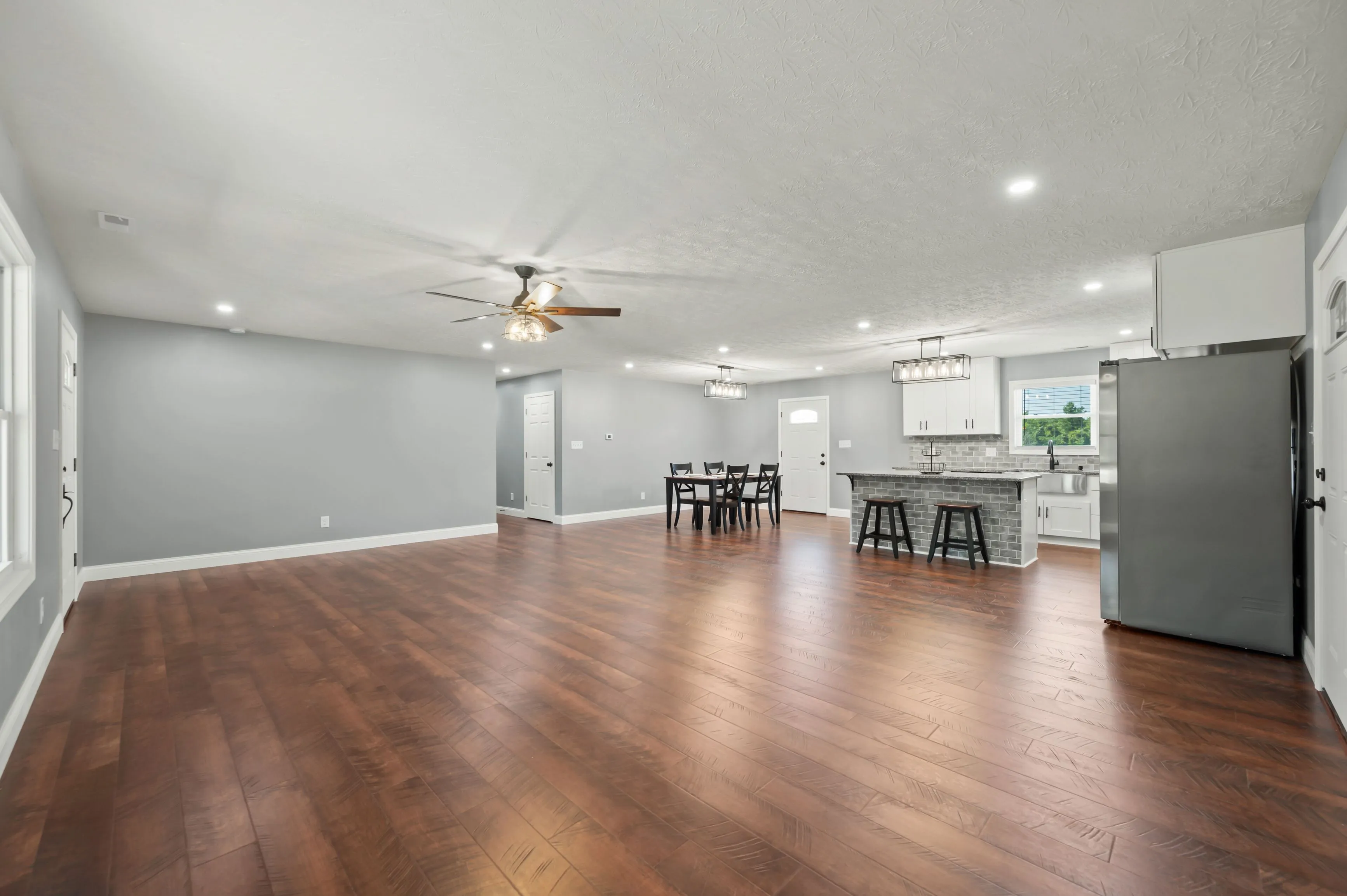 Spacious, modern kitchen with stainless steel appliances, white cabinetry, and a dining area with a dark wooden table set on polished hardwood flooring.