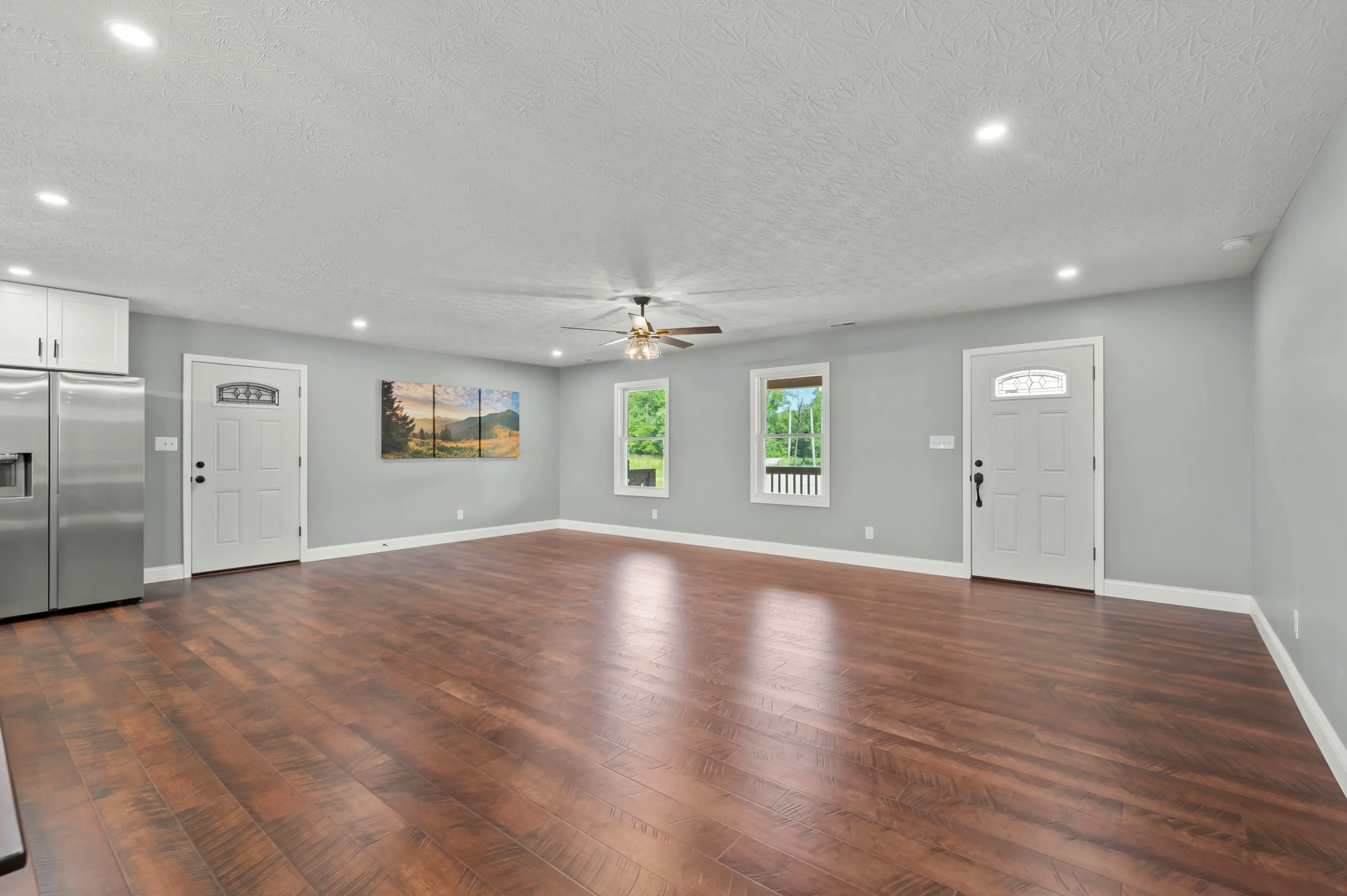 Spacious modern room with polished hardwood floors, gray walls, white doors, a ceiling fan, and a framed landscape painting.
