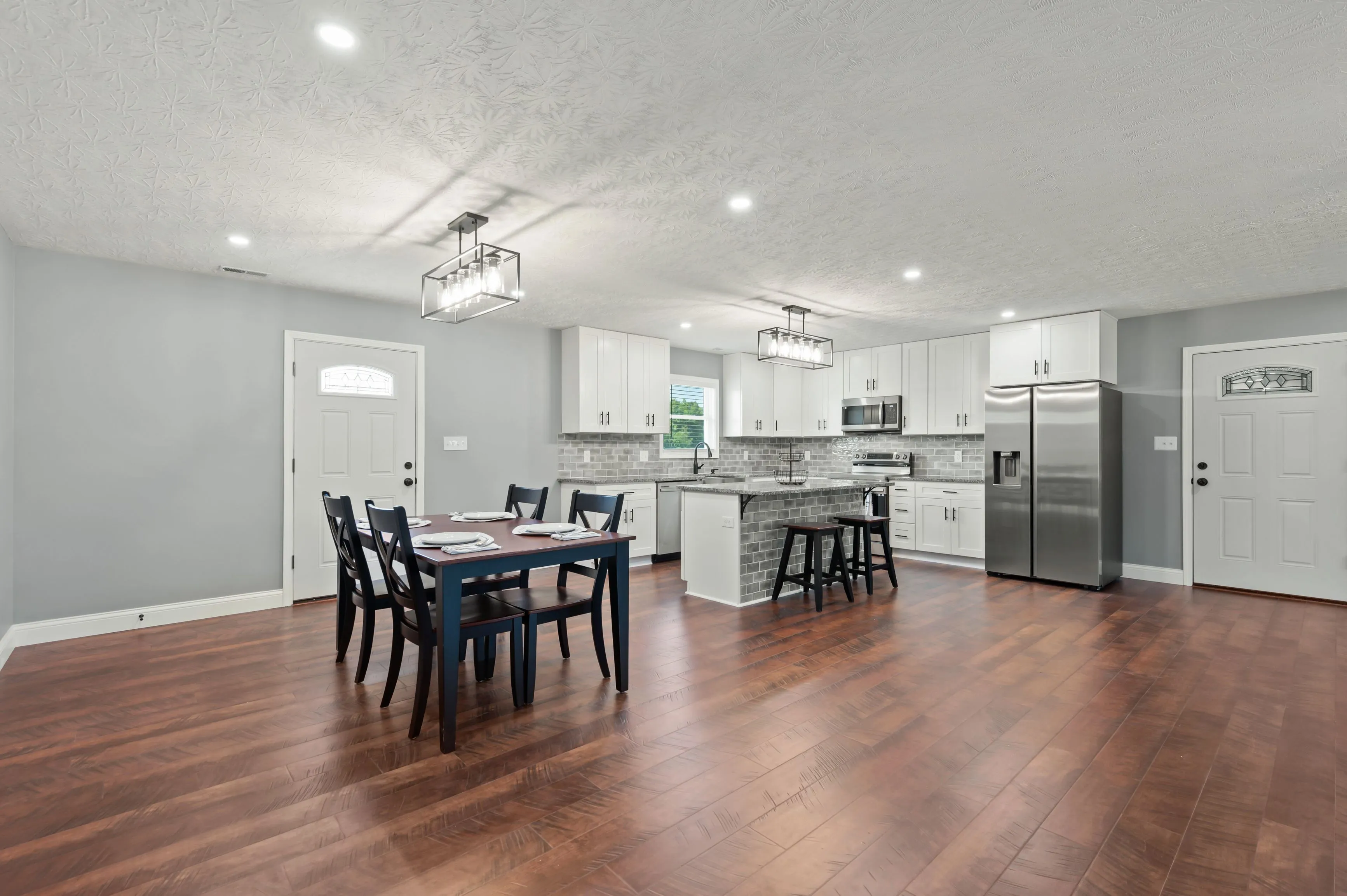 Modern spacious kitchen and dining area with gray walls, stainless steel appliances, white cabinets, a dining table set, and hardwood flooring.