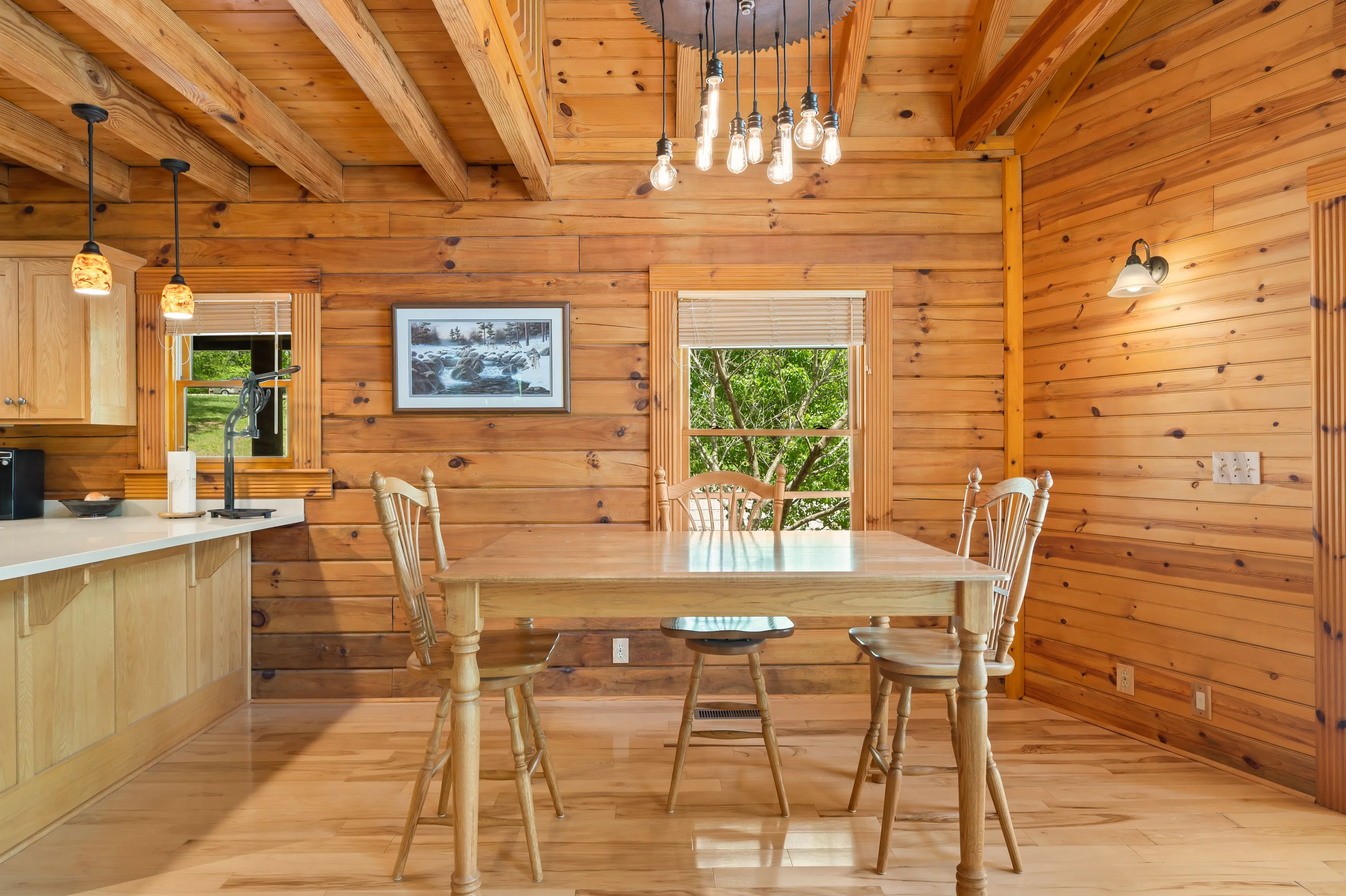 Interior of a cozy wooden cabin kitchen with dining table, chandelier, and kitchen counter.