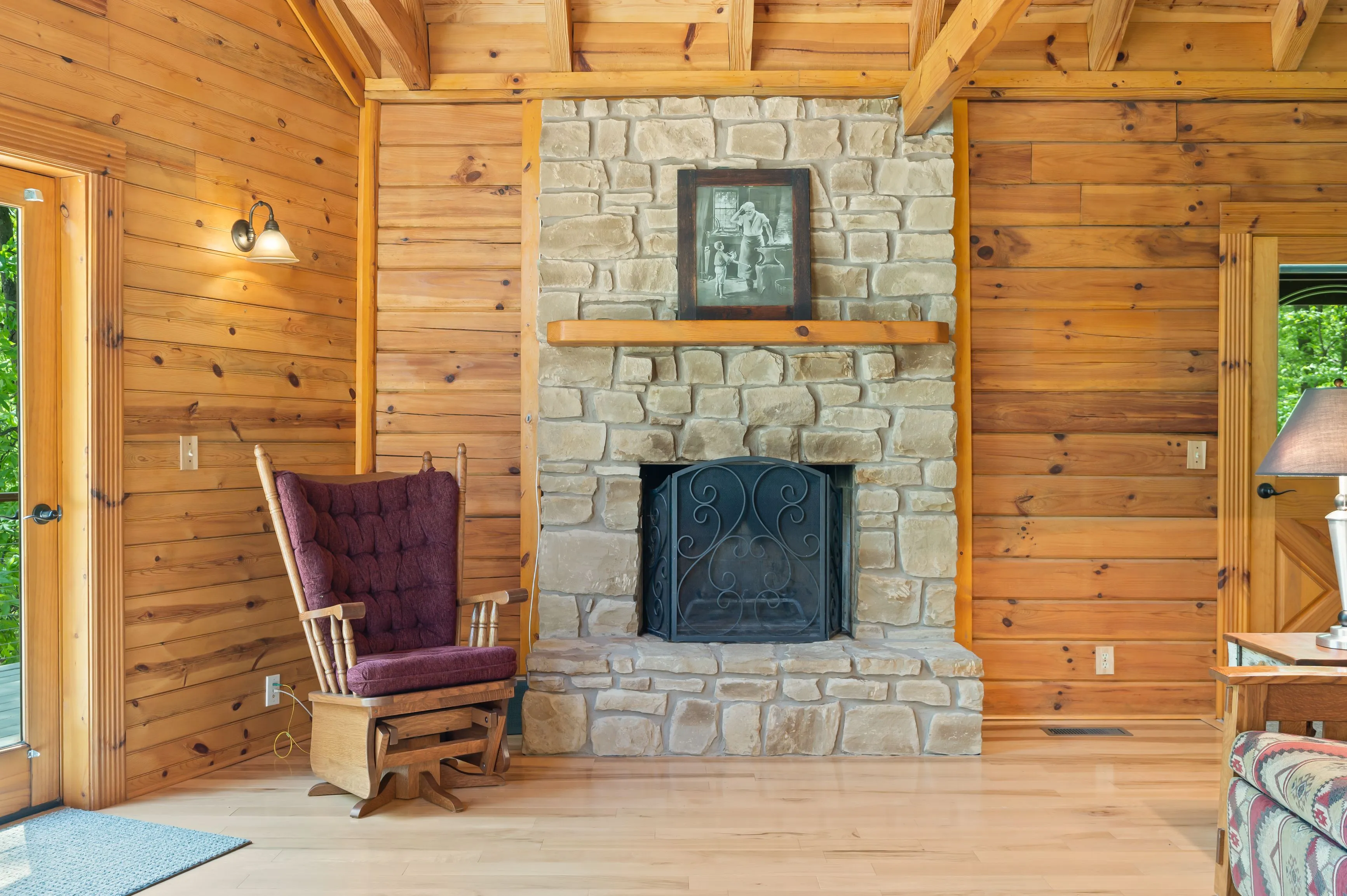Cozy cabin interior with wooden walls and beams, a stone fireplace, and a vintage armchair.