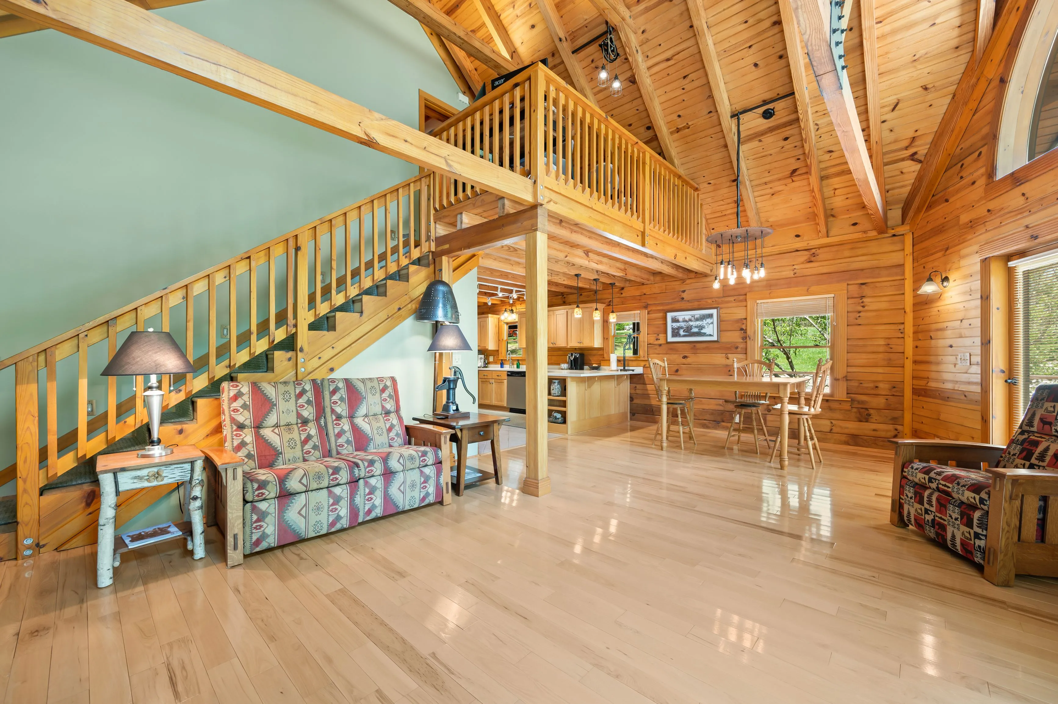 Interior of a spacious log cabin with a high ceiling, wooden stairs leading to a second level, and rustic furniture.