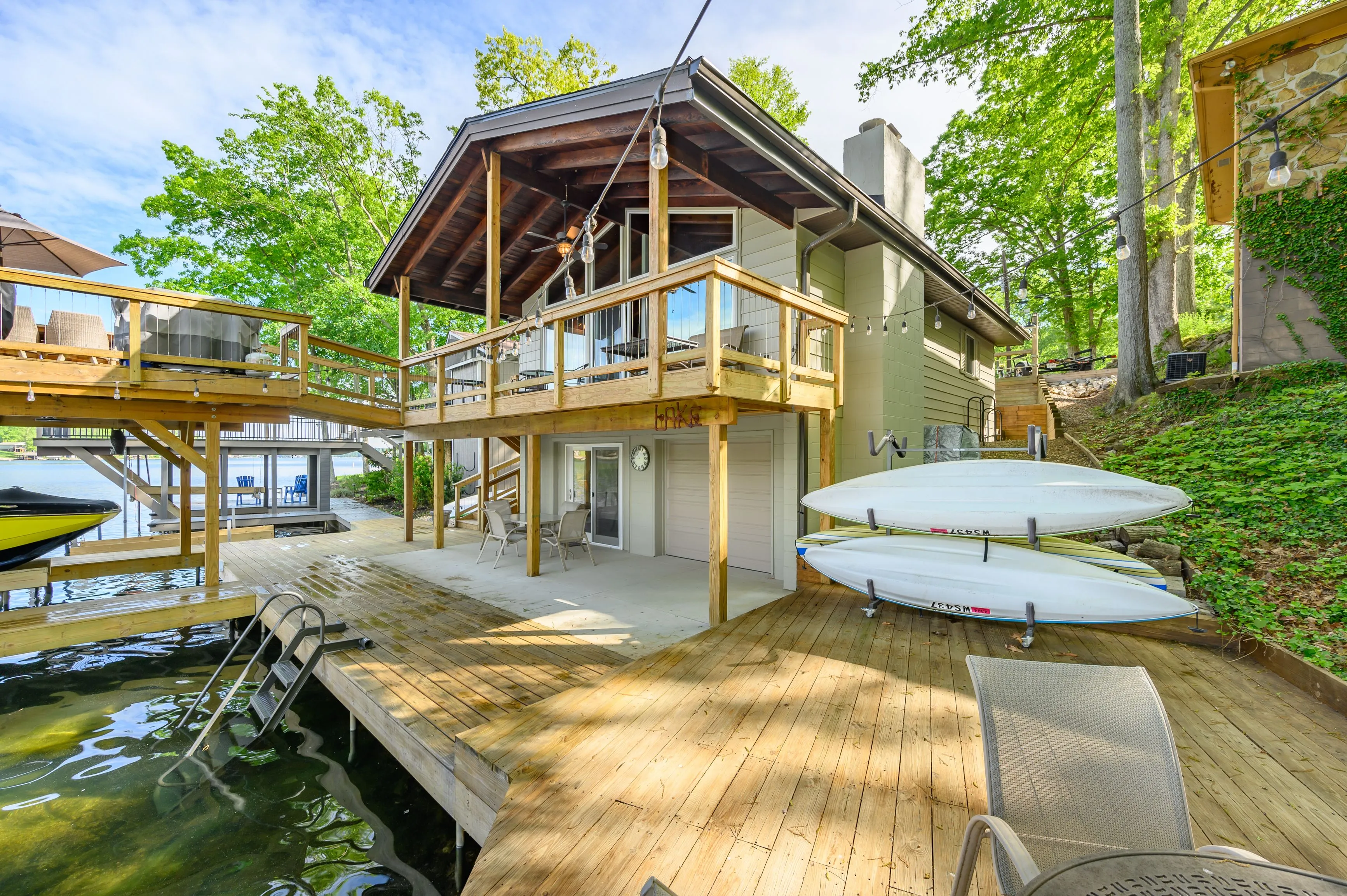 Lakeside house with a boat dock and multiple decks among green trees on a sunny day.