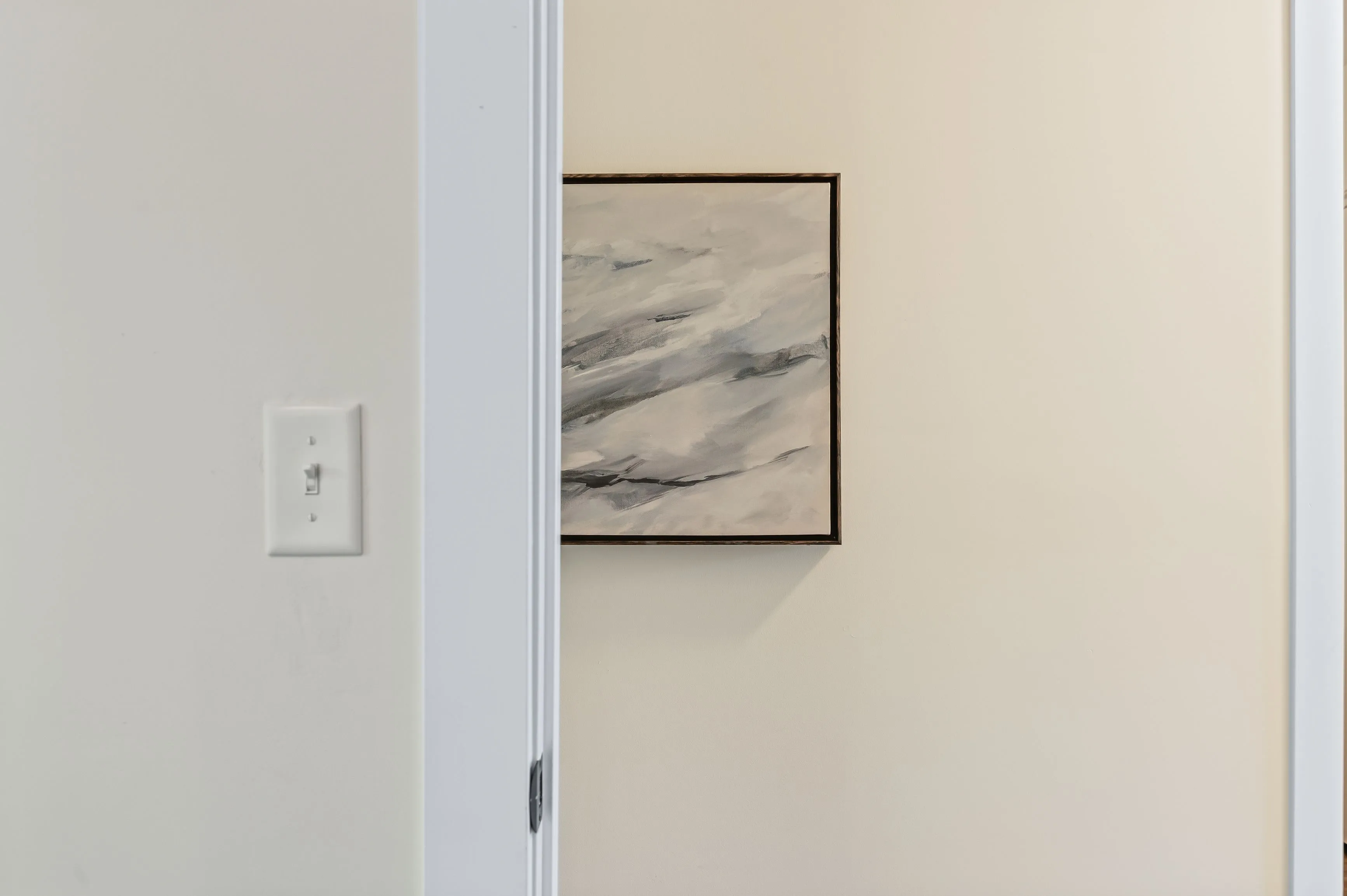 Interior wall with an abstract monochrome artwork hanging next to an open door, with a light switch on the left.