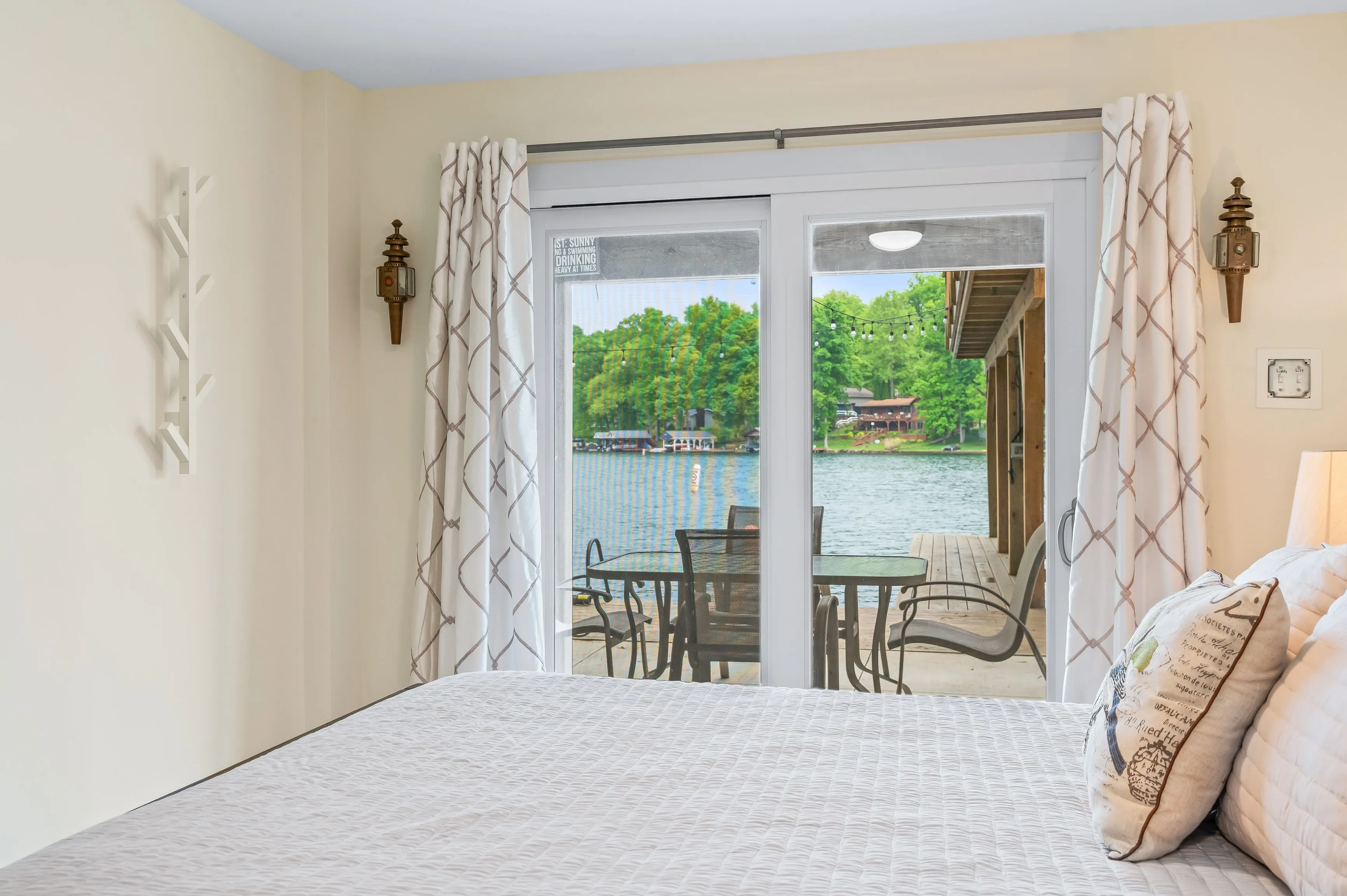Lake view from a cozy bedroom with glass doors leading to outdoor patio with seating area.