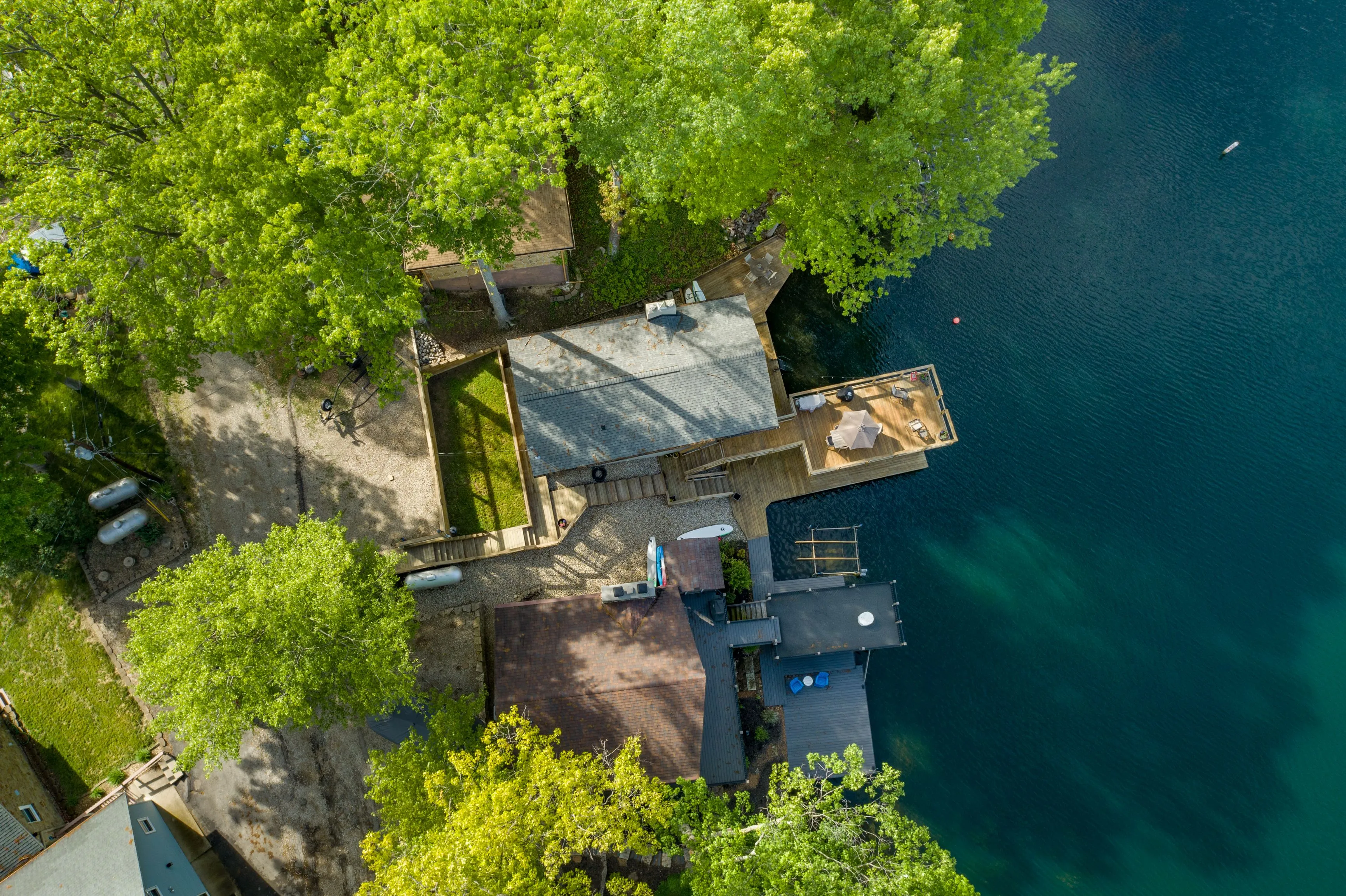 Aerial view of a lakeside house with a dock surrounded by lush trees.