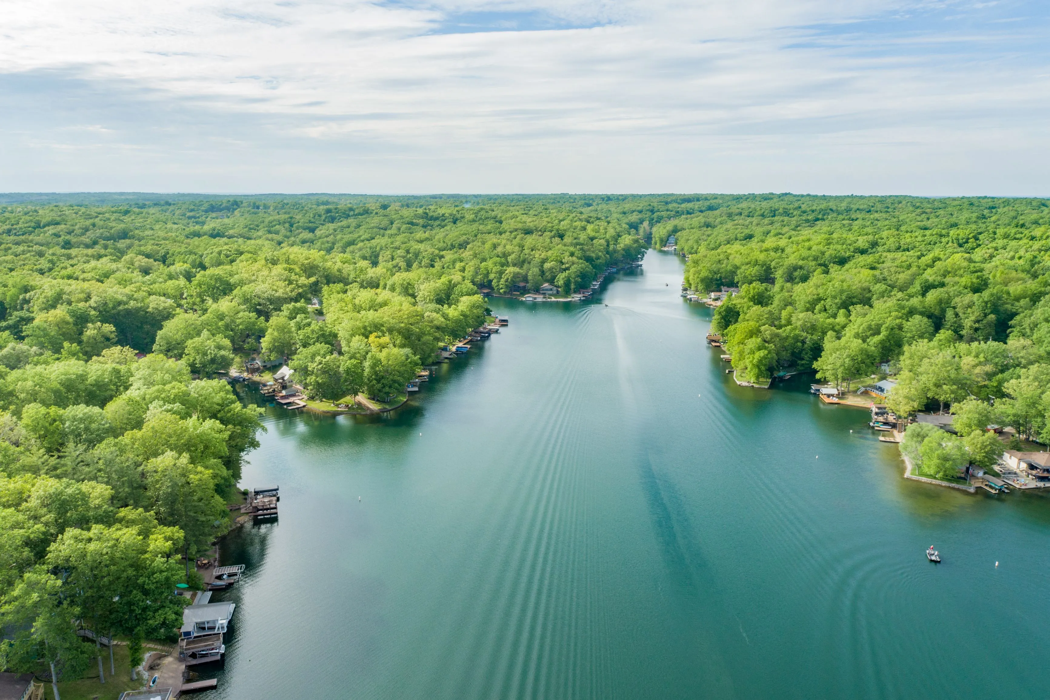 Aerial view of a serene river flowing through a lush green forest with docks along the banks.