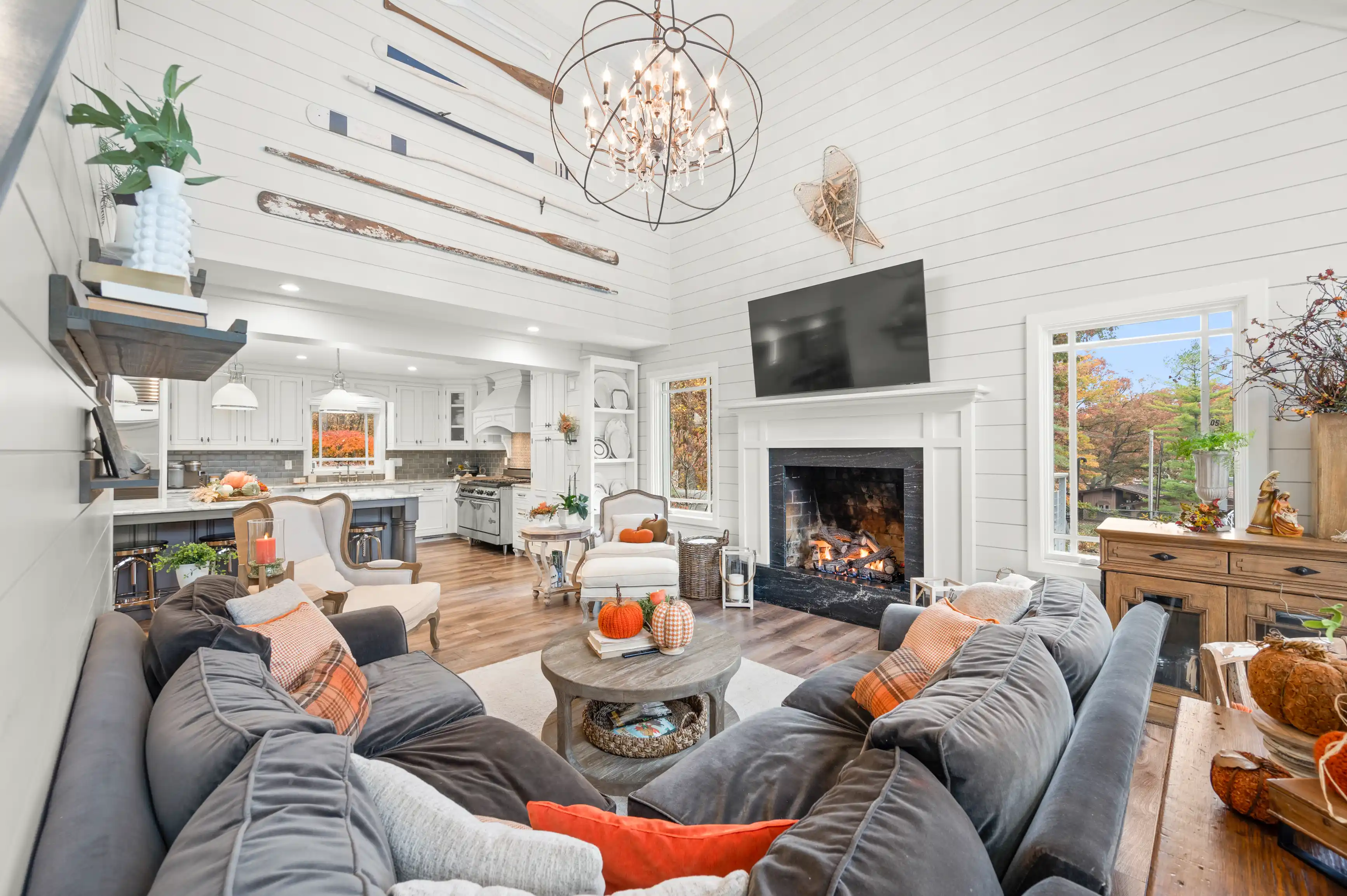 Spacious, bright living room with a cozy fireplace, comfortable seating, and an open concept kitchen in the background, decorated with warm, autumnal accents.