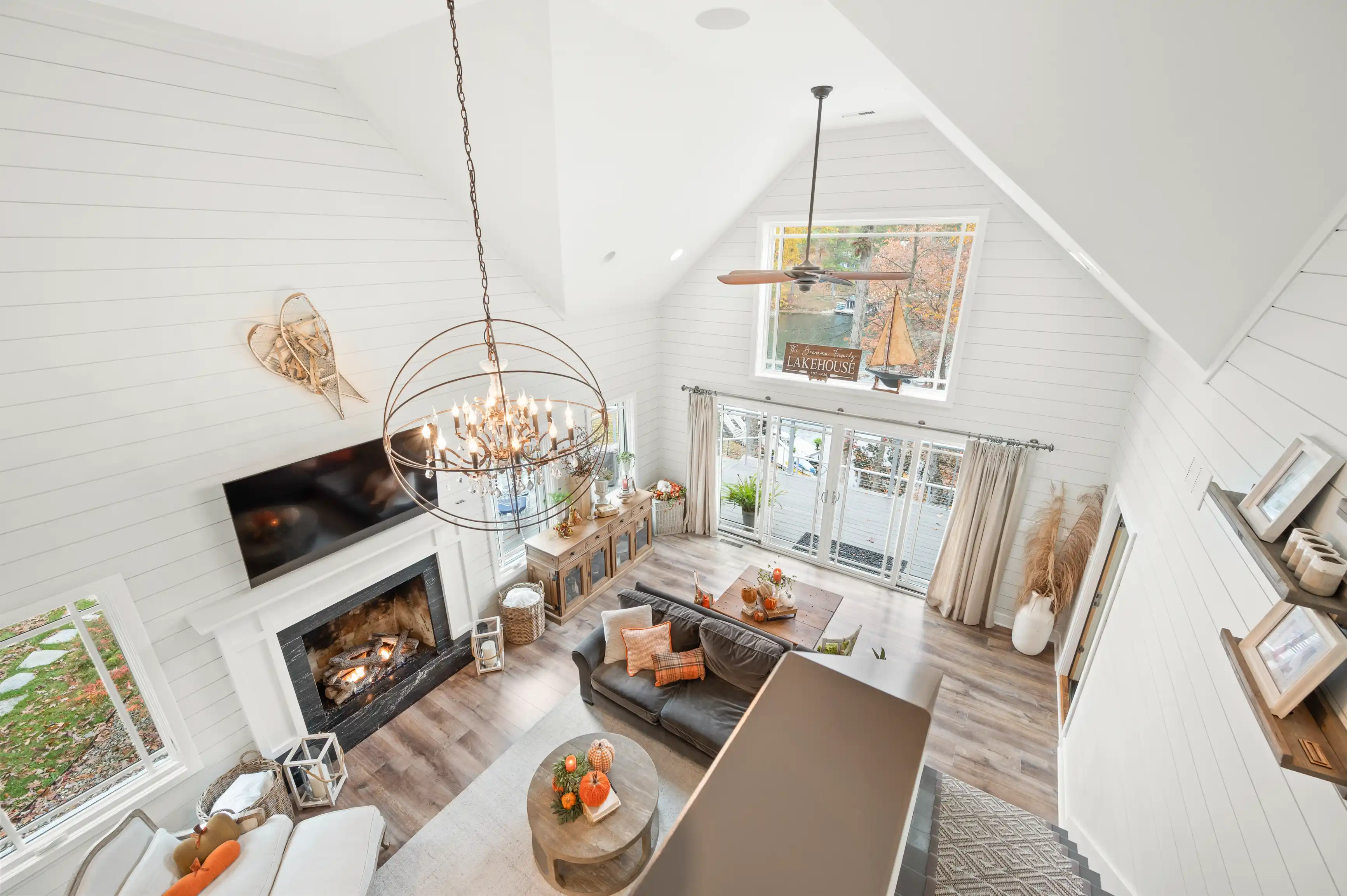 Bright, airy living room with vaulted ceilings, modern chandelier, fireplace, and French doors opening to a balcony, with autumnal decor touches.
